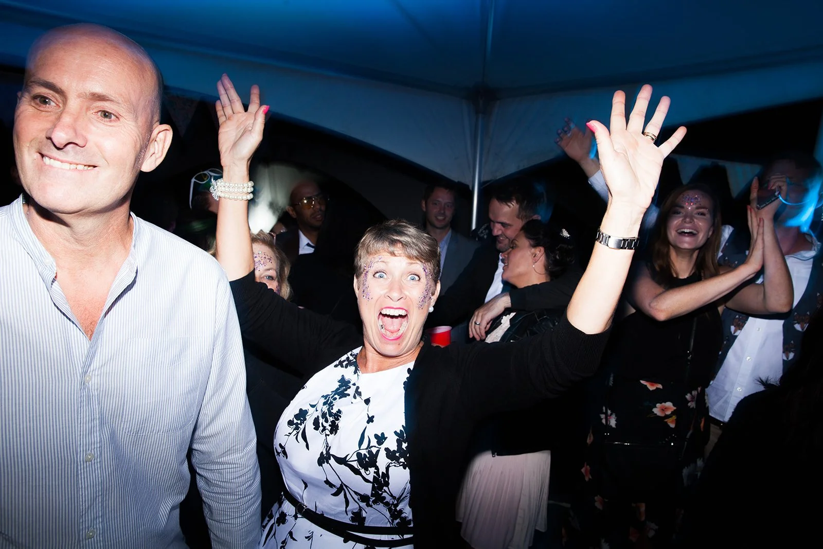 People dancing and celebrating at a party, with colorful lighting and lively expressions.
