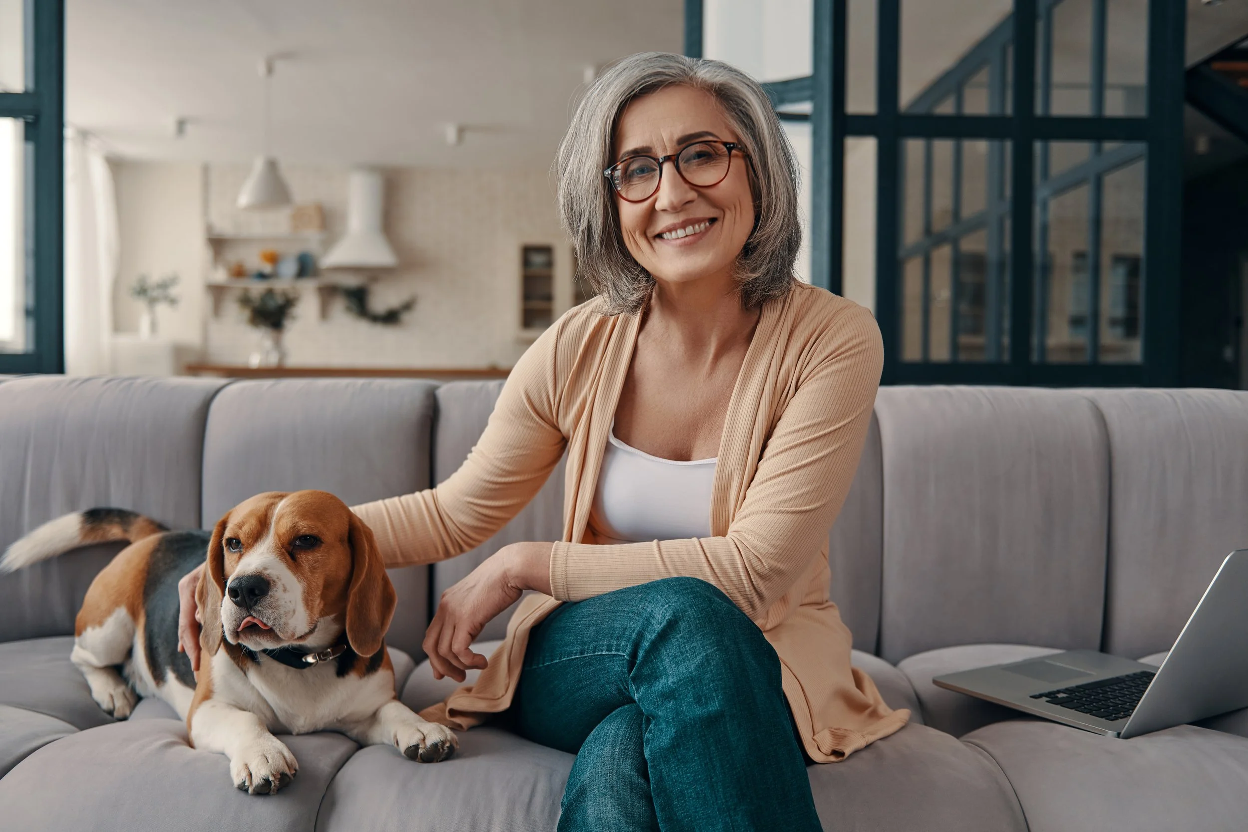 Image of woman on her sofa, smilling and petting her dog.