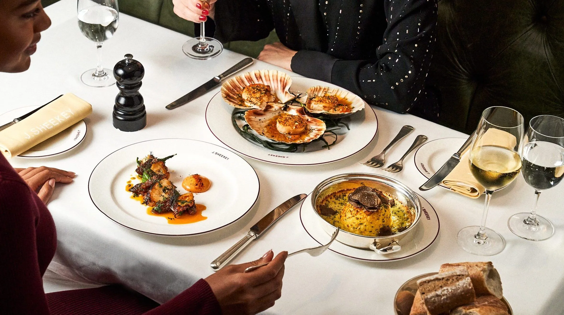 People dining at a restaurant table with plates of seafood, including scallops and clam shells, and glasses of wine.