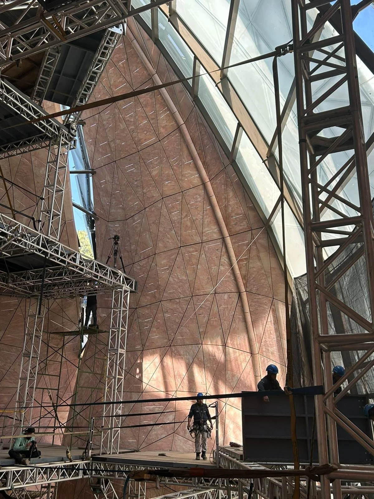 Construction workers and scaffolding inside a large, modern building with curving stone walls and large glass windows. Mexico City rosa portugallo