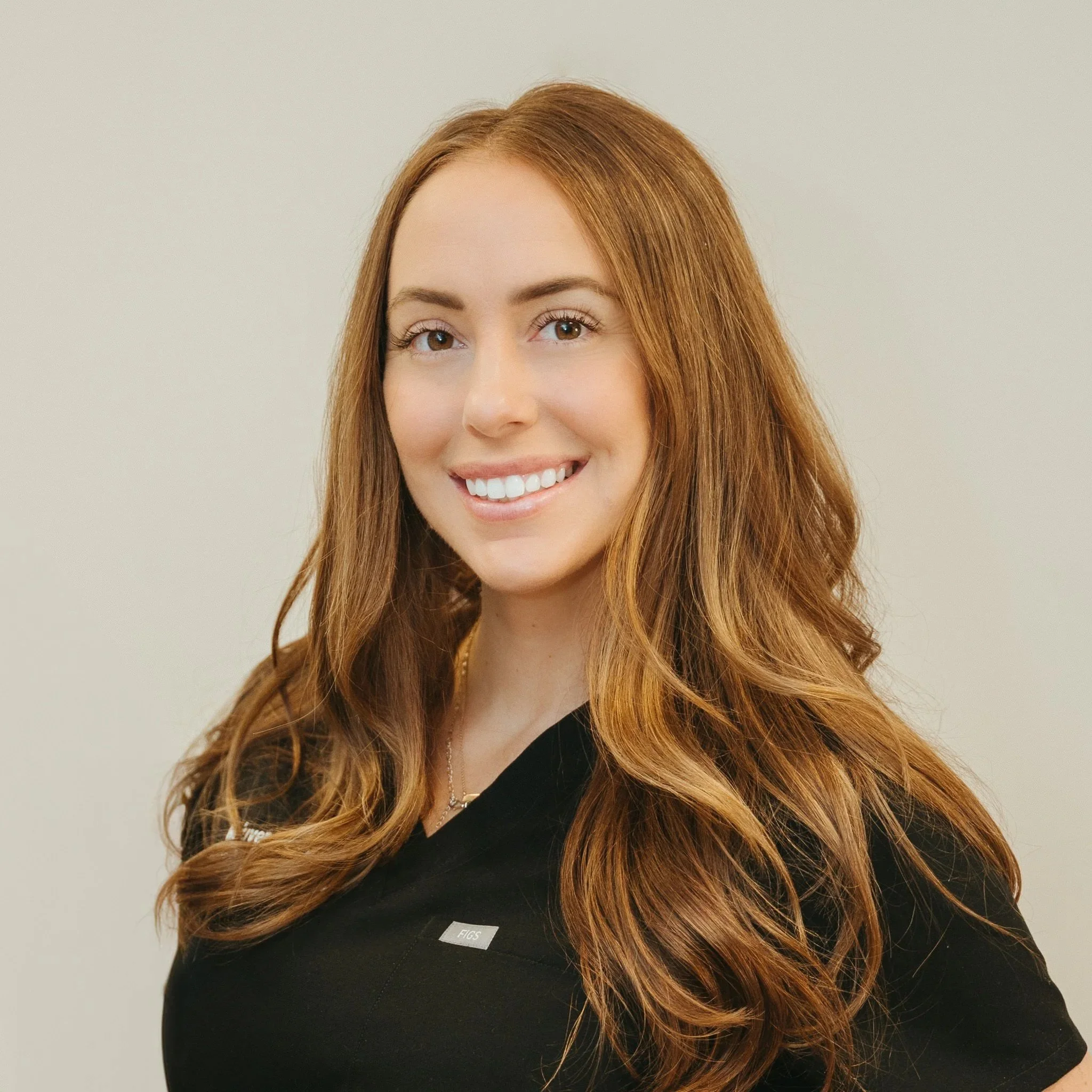 Portrait of a young woman with long, wavy red hair smiling, wearing a black uniform with a small nametag.