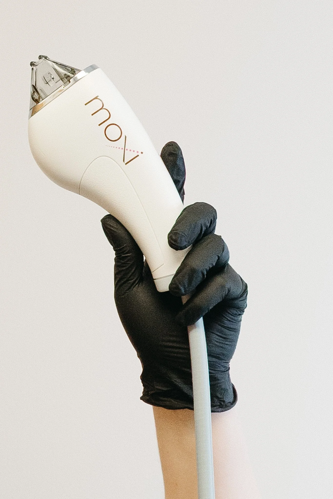 A hand wearing a black glove holding a MOXI device against a plain white background.