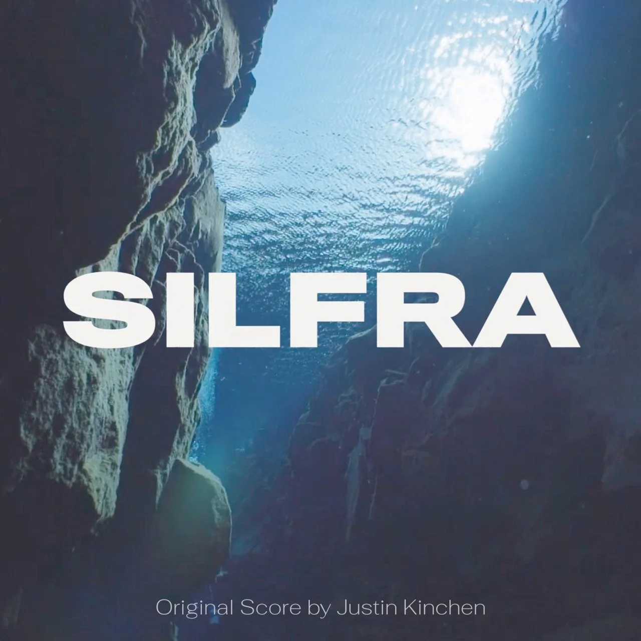 Sunlit view of water through a rocky opening, with the word 'SILFRA' in large white letters and text indicating the original score by Justin Kinchen.