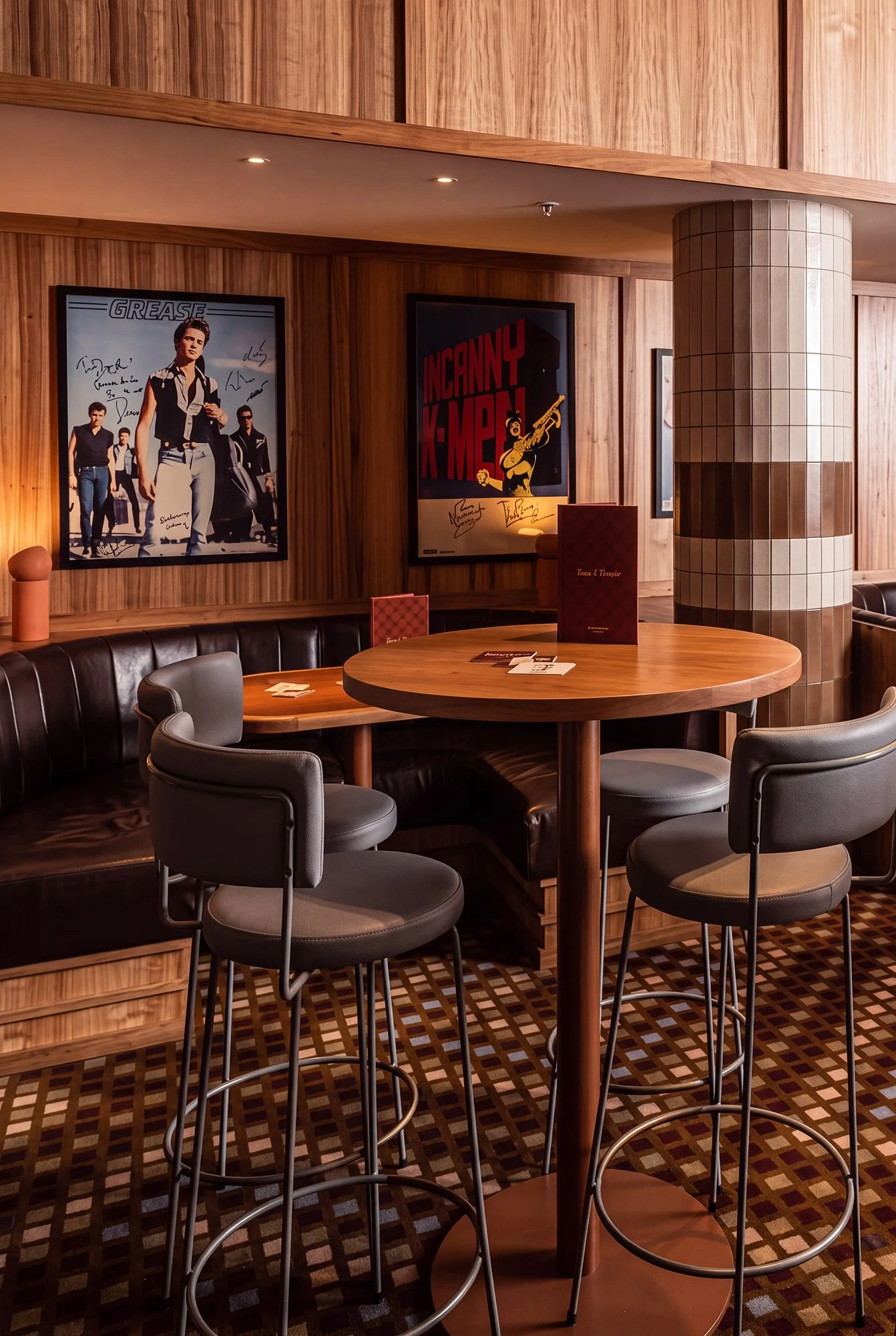 A round wooden table with four chairs in a restaurant or lounge with wood-paneled walls and framed posters, including one of pop singer Britney Spears.