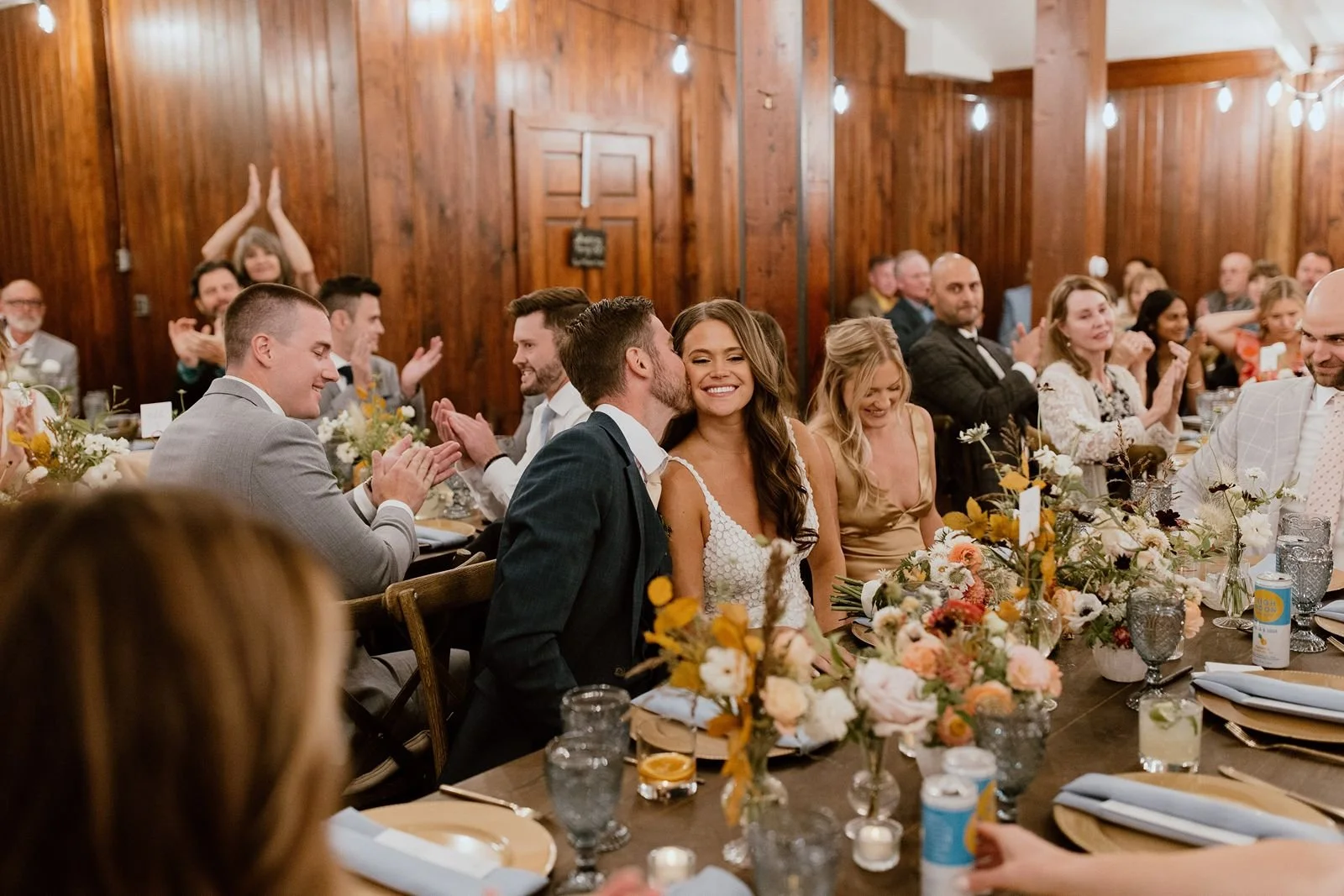 Groom kissing bride's cheek in intimate barn at reception in Steamboat Springs