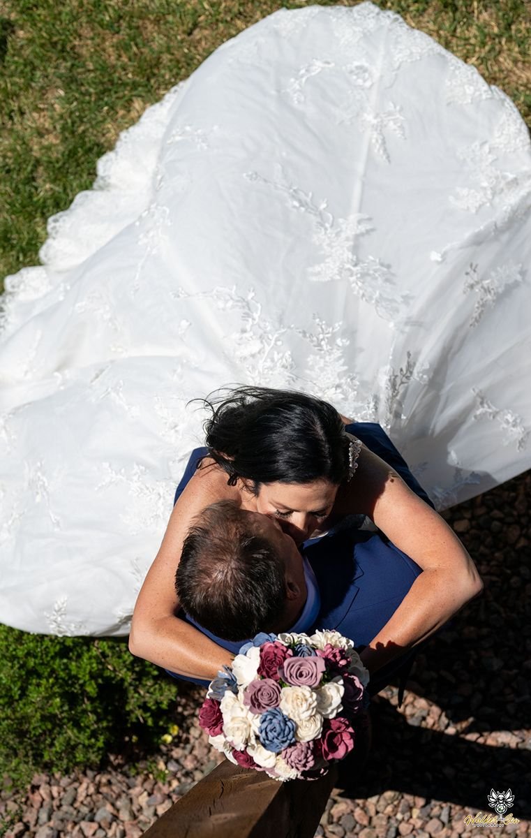 Bride holding bouquet over groom's head while photographer looking down on them