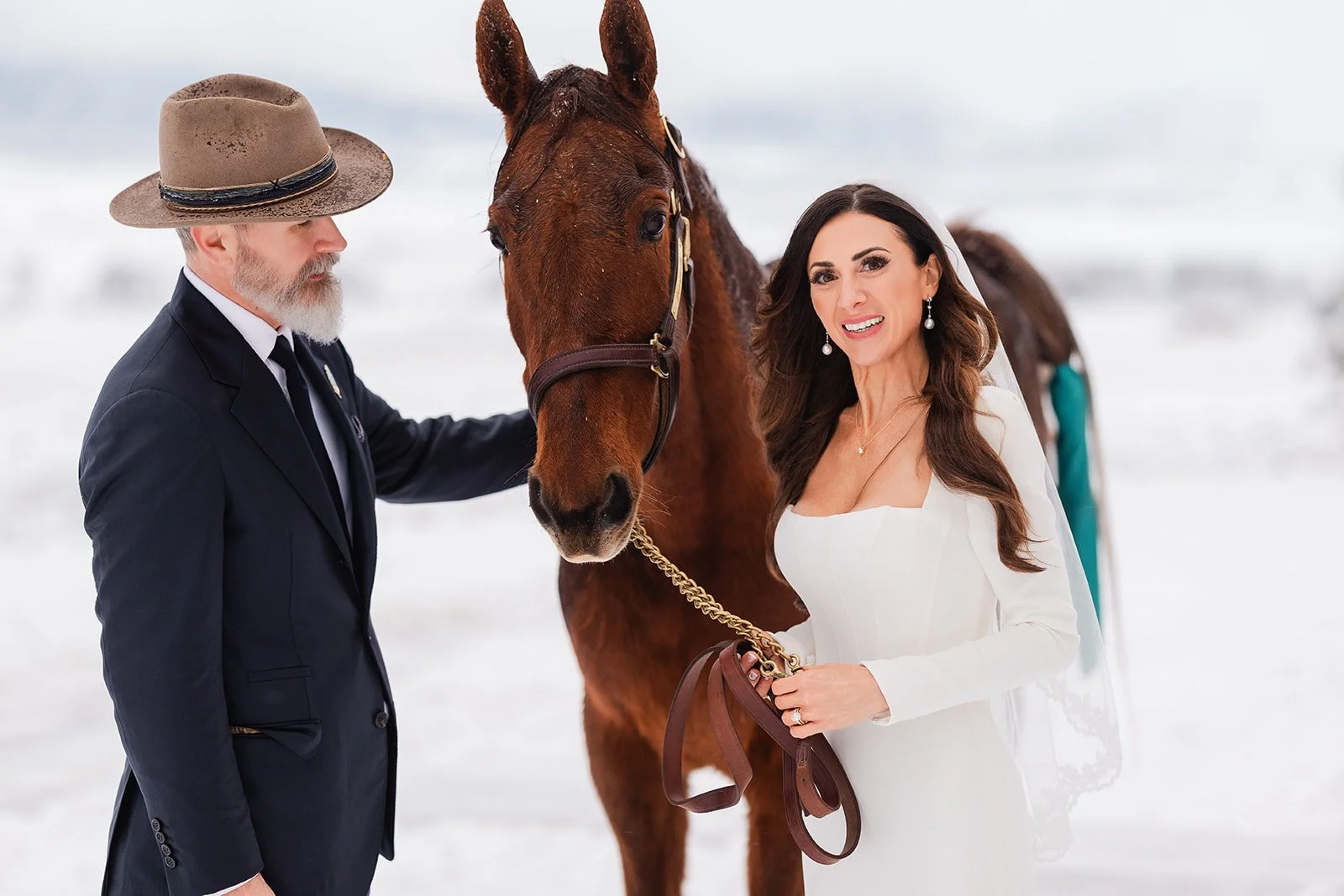 Couple standing with horse in the snow at luxury winter wedding at destination ranch in Steamboat Springs, Colorado