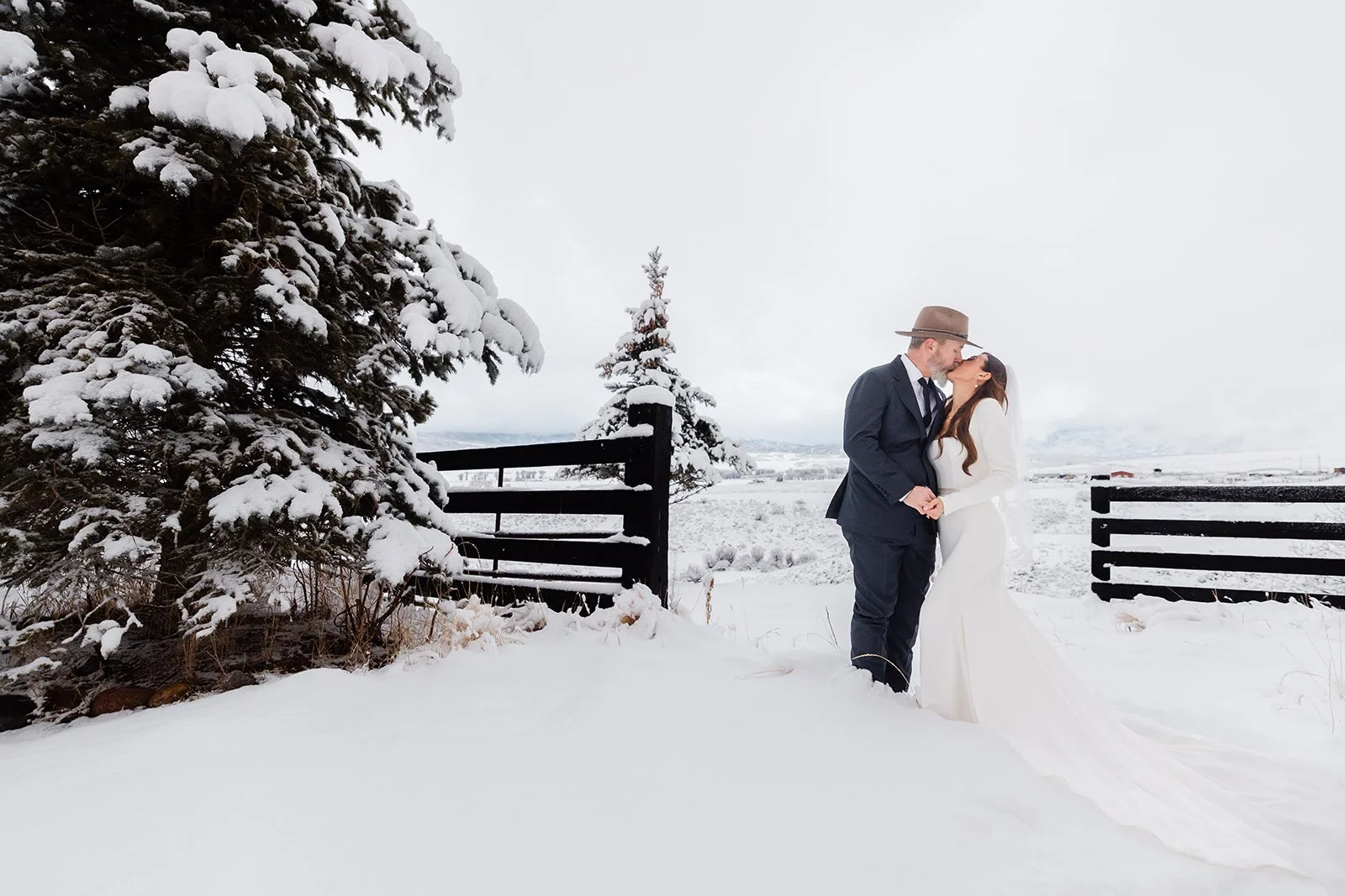 Couple kissing after winter wedding in snow by the trees in Steamboat Springs at luxury ranch wedding