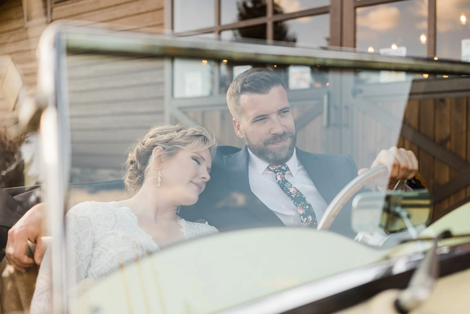 Bride resting her shoulder on groom who is driving a vintage car for their winter elopement at La Joya Dulce in Steamboat Springs, Colorado.