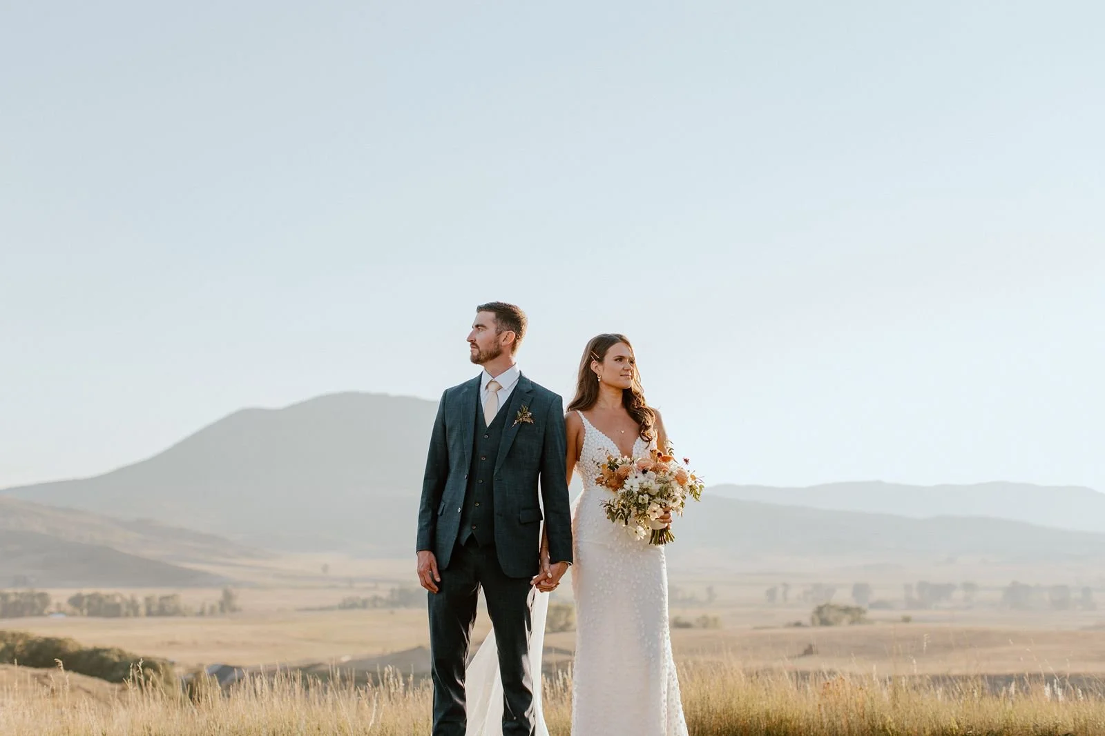 Newly married couple holding hands with mountains in background at luxury ranch in Steamboat Springs, Colorado