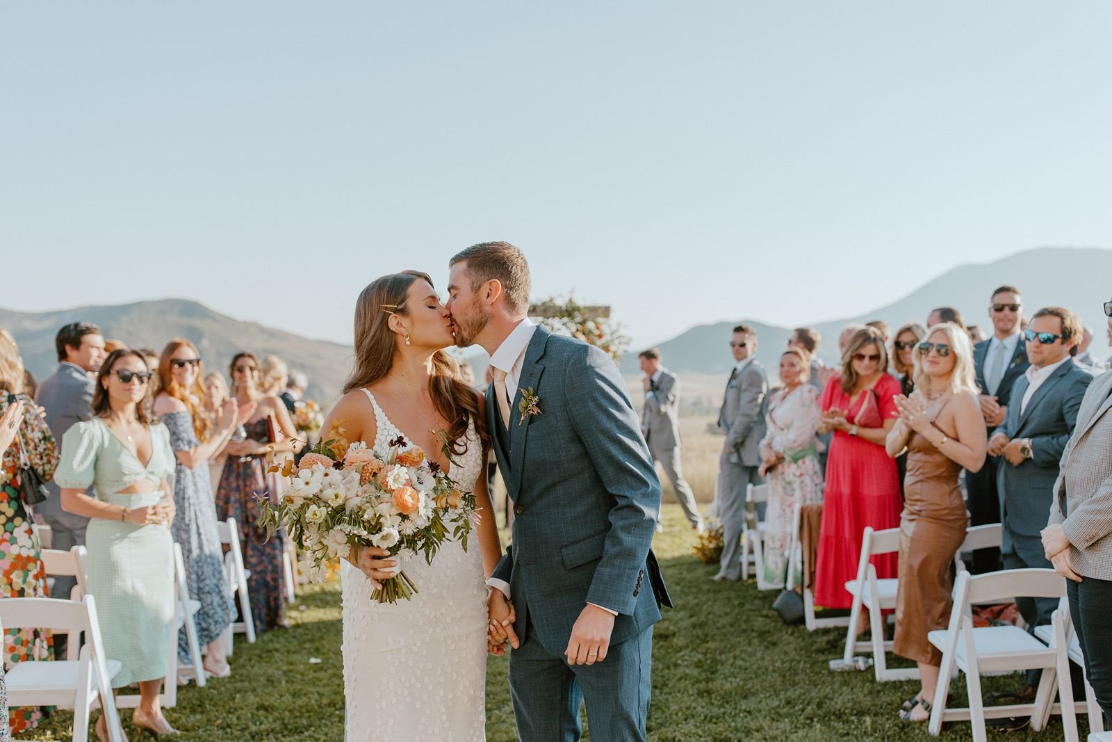 Newly married couple sharing kiss walking down the aisle at luxury ranch wedding venue in Steamboat Springs