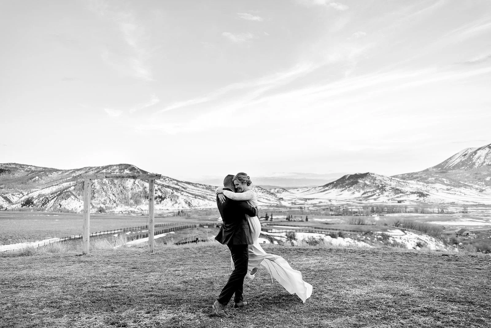 Groom lifting and twirling bride with mountains and snow in background at their winter elopement at La Joya Dulce in Denver, Colorado