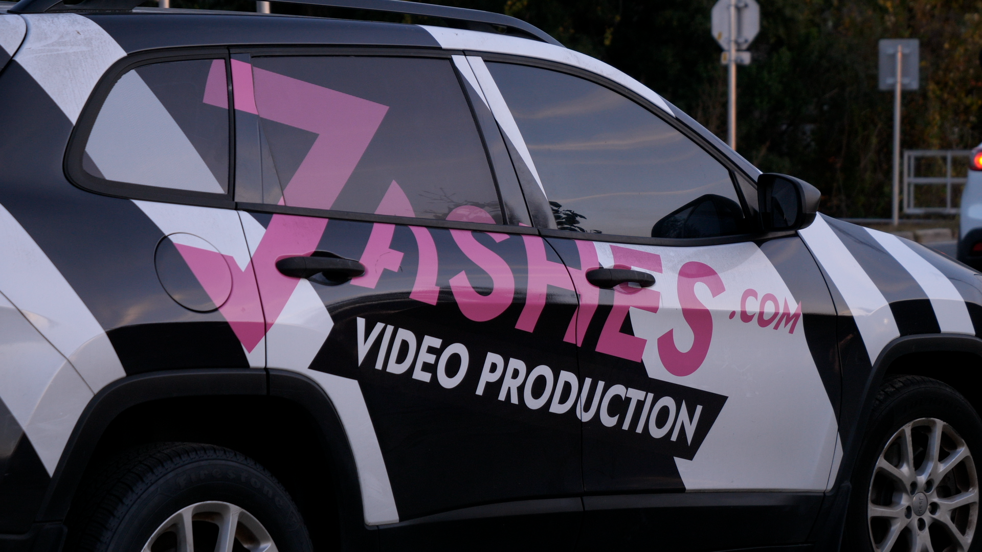 Vehicle wrapped with advertisement for a video production company, featuring pink text that reads 'ZASHES.COM' and white text 'VIDEO PRODUCTION' on a black background.