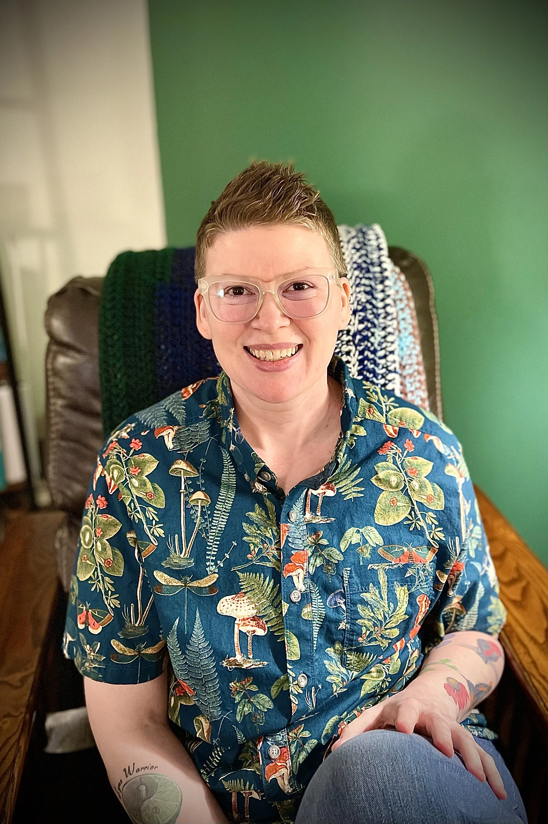 a black and white photo of loey smiling. they have black framed glasses and short blonde hair.