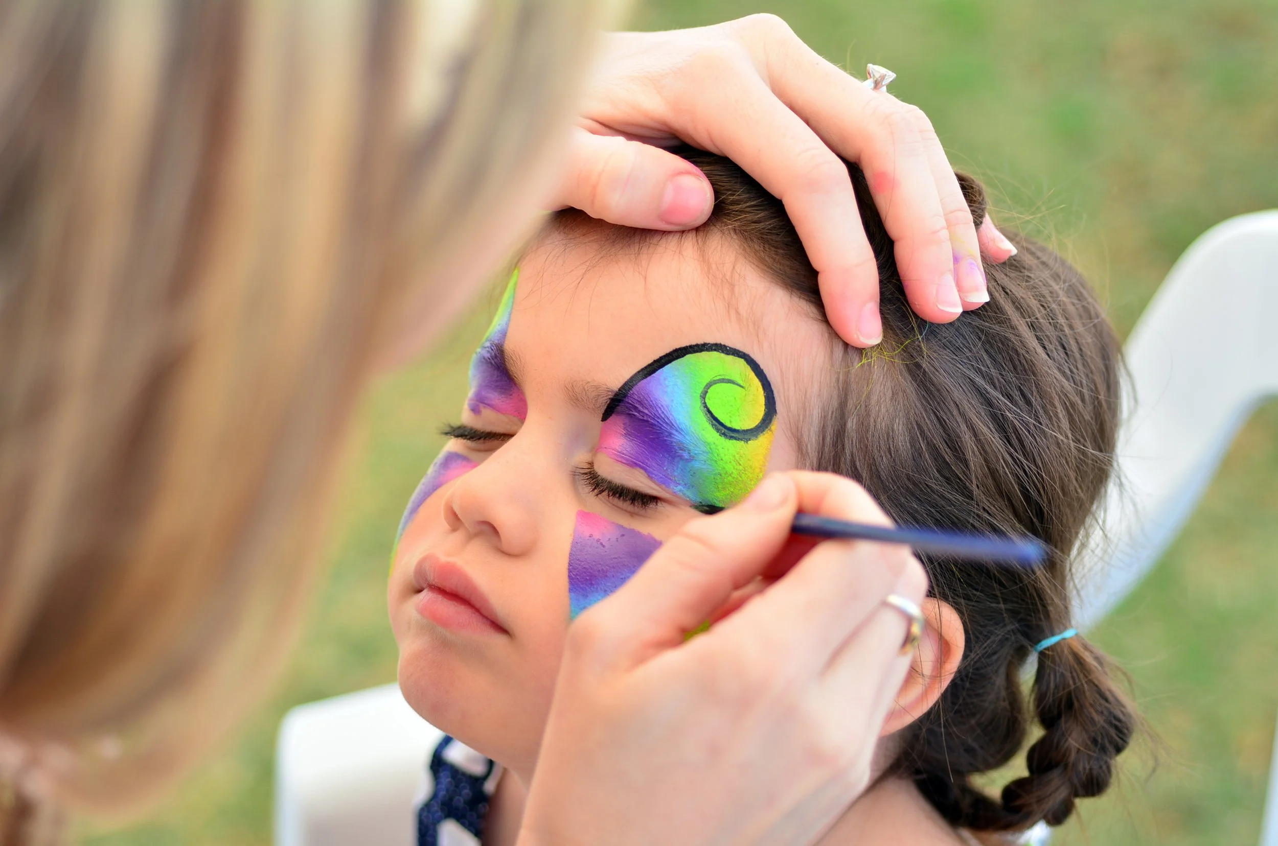 Girl getting her face painted with vibrant colors.