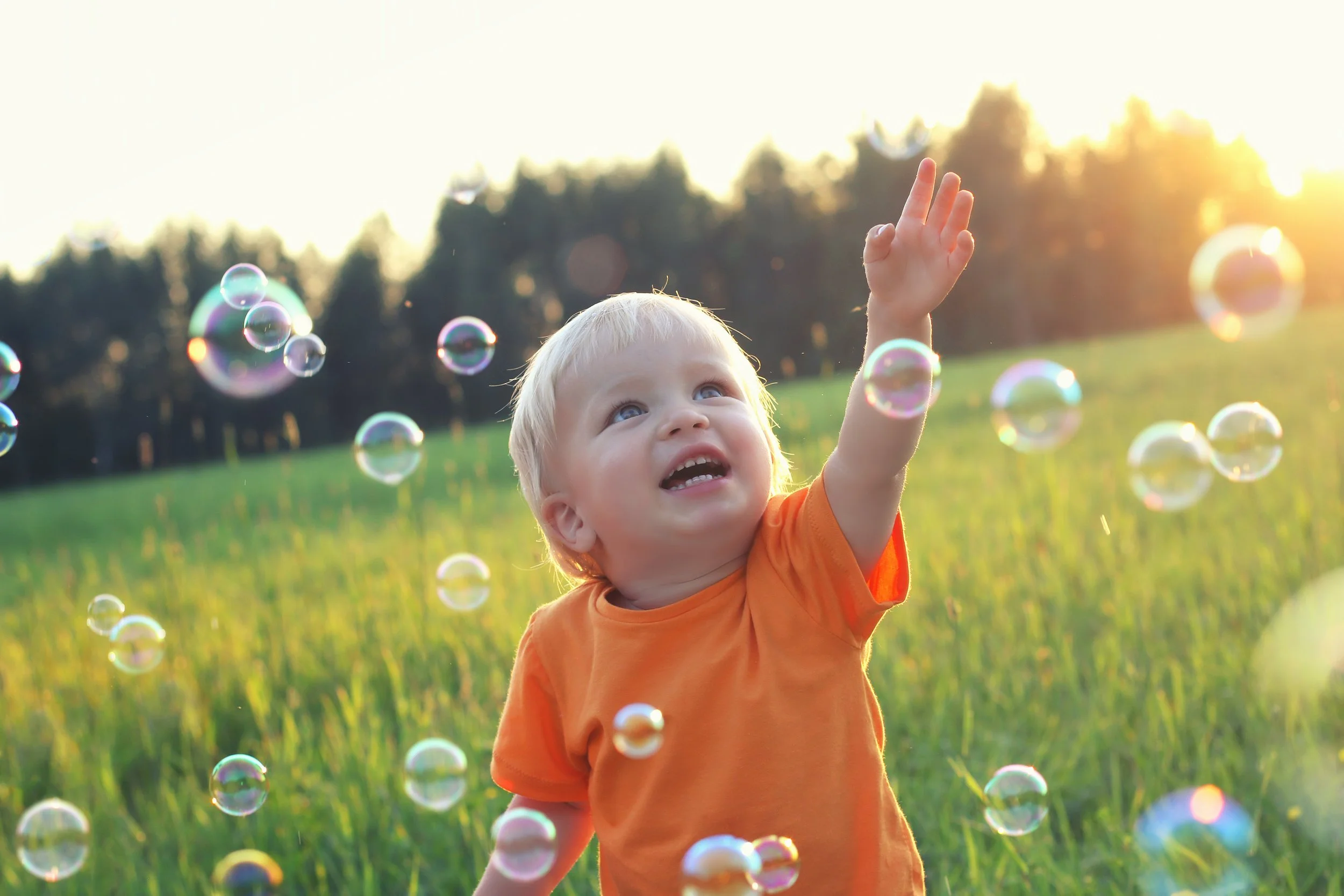 Child surrounded by bubbles trying to pop bubbles.