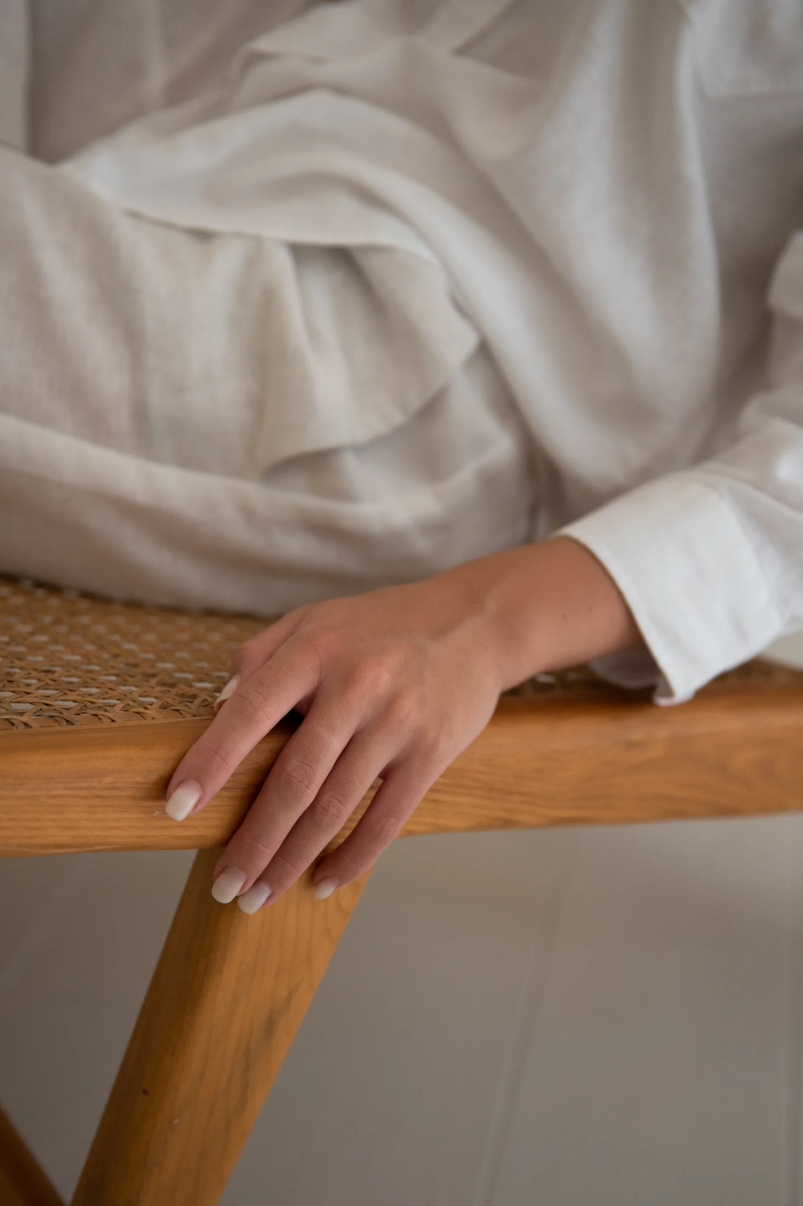 Close-up of a person's hand resting on a wooden table with a woven surface, wearing a white long-sleeve shirt.