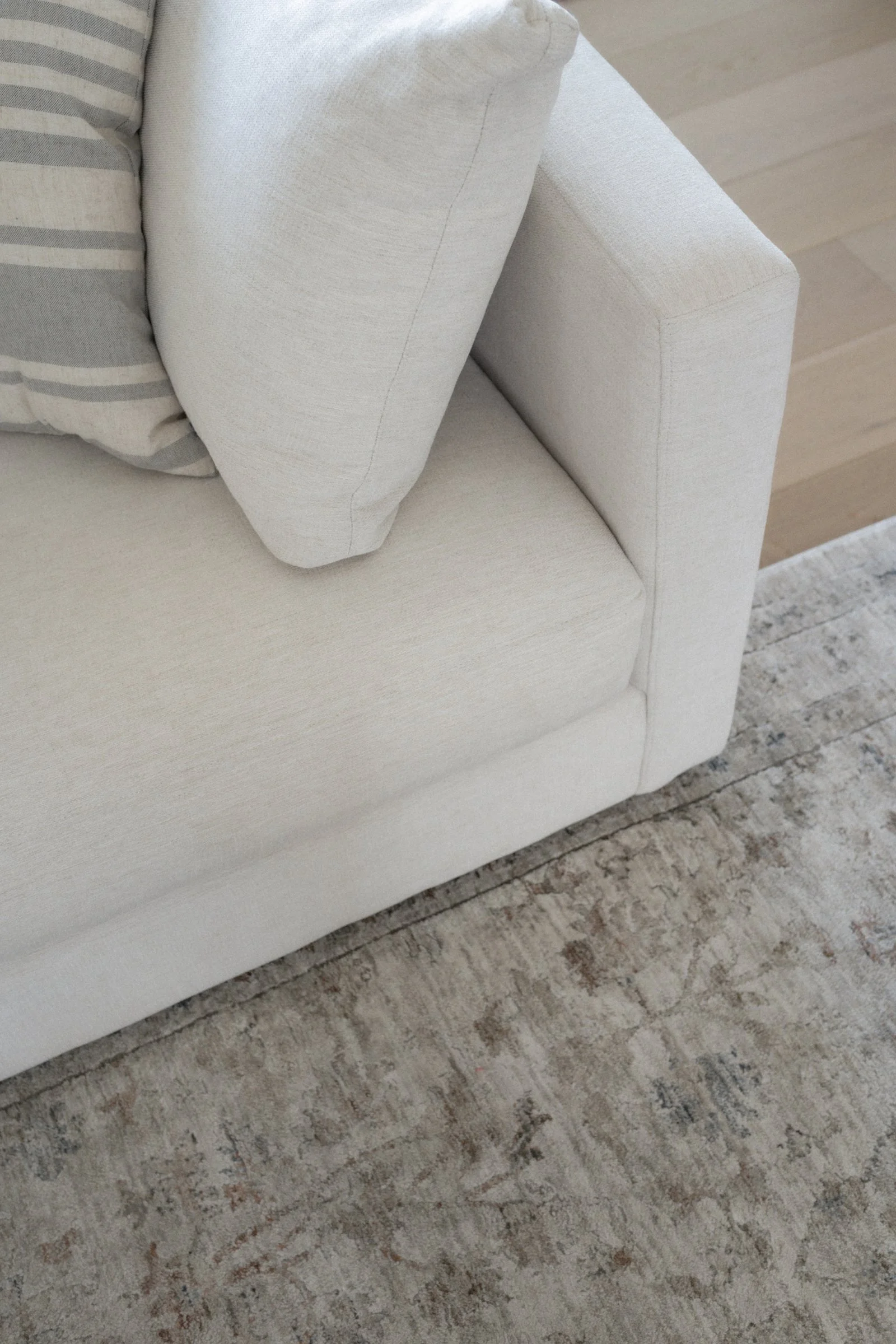 Close-up of a white sofa with a decorative pillow on it, situated on a stone or tile floor.