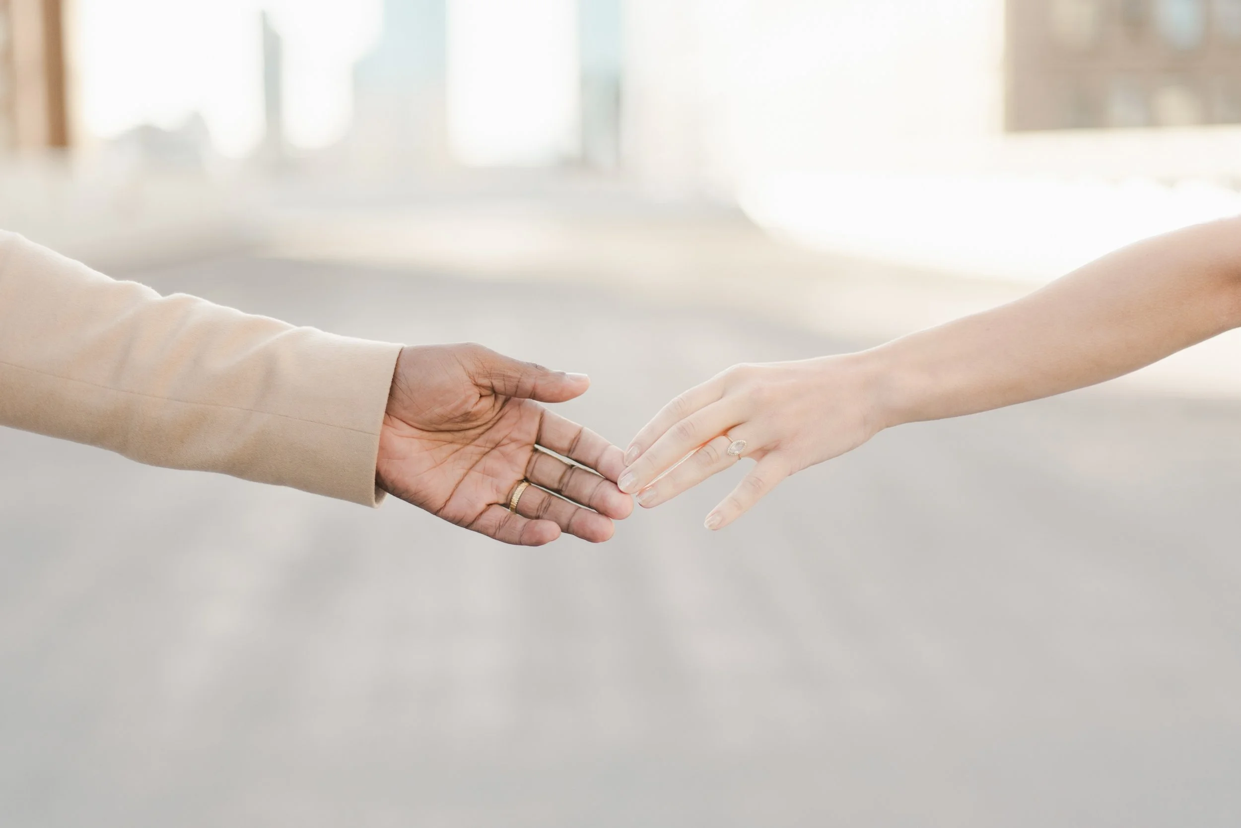 Two people holding hands, with one person's hand reaching out to the other in a gentle grasp.