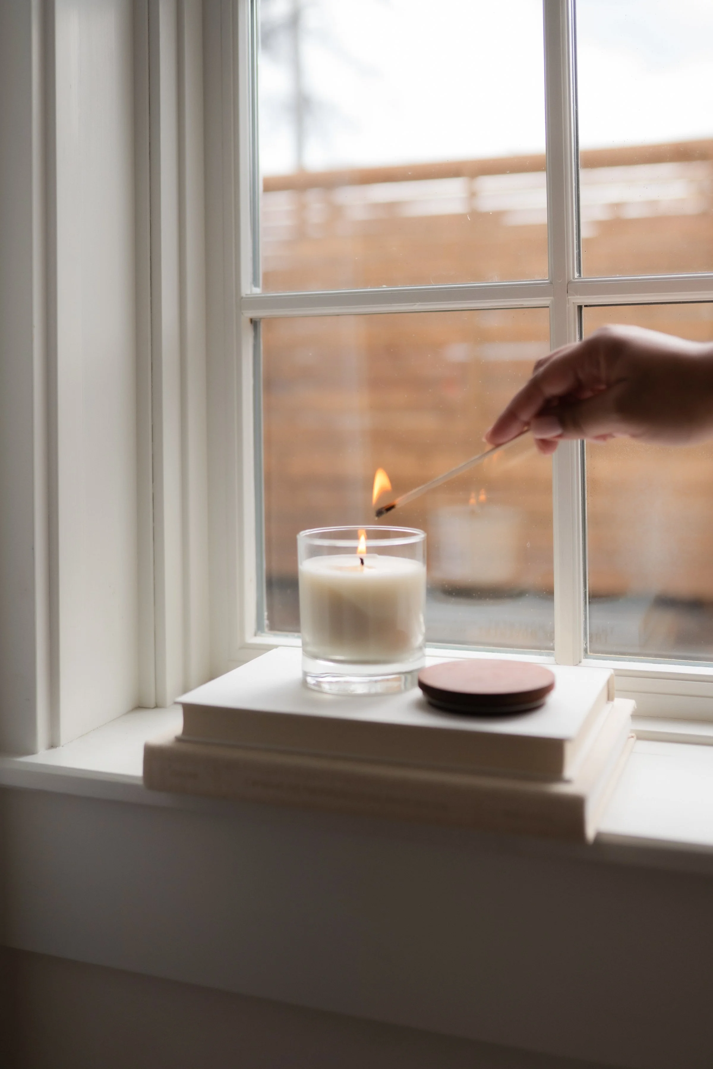 Person lighting a candle on a windowsill with a matchstick
