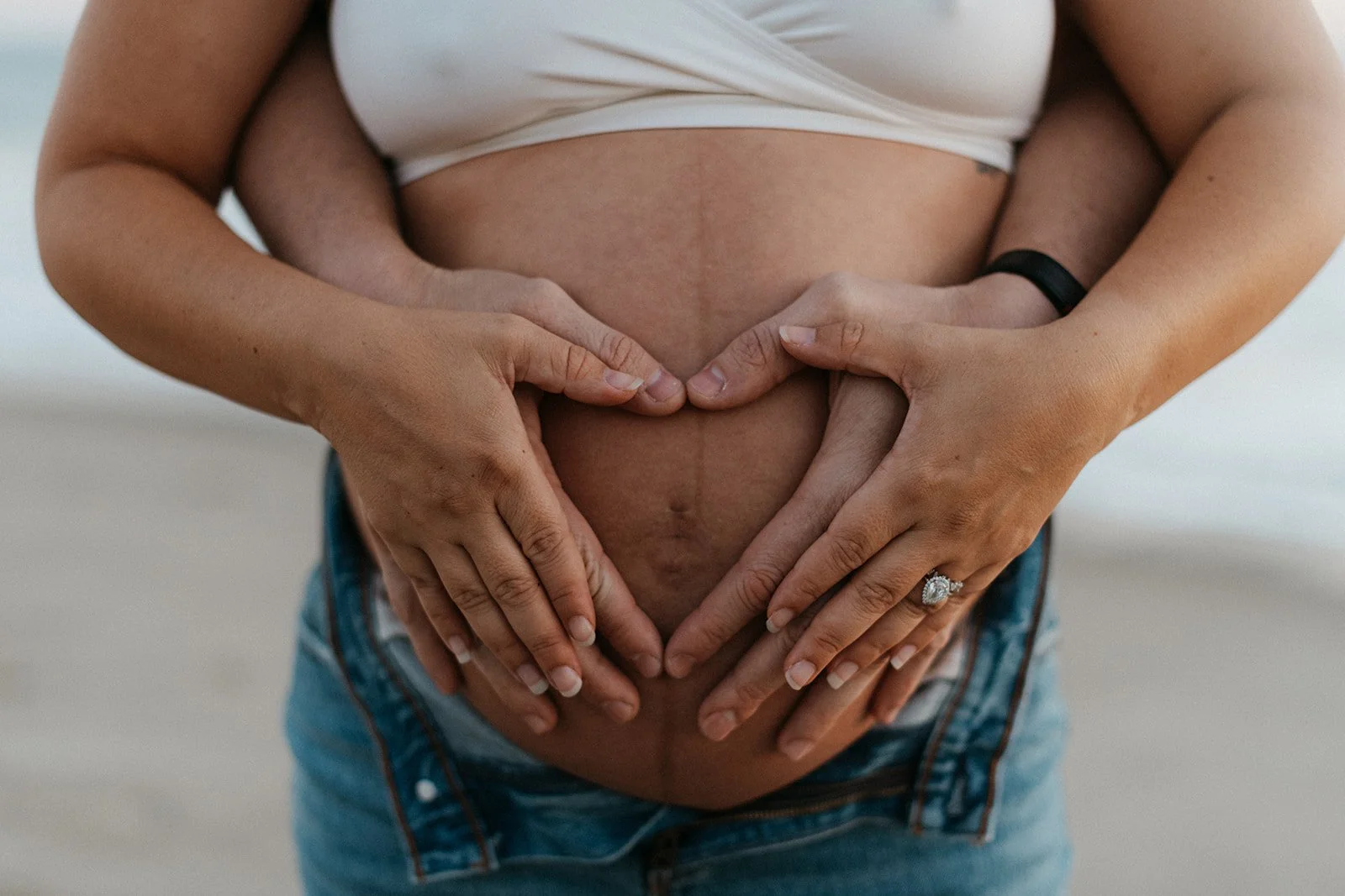 A pregnant woman with her partner making a heart shape with their hands on her belly.Preparing for HypnoBirthing.