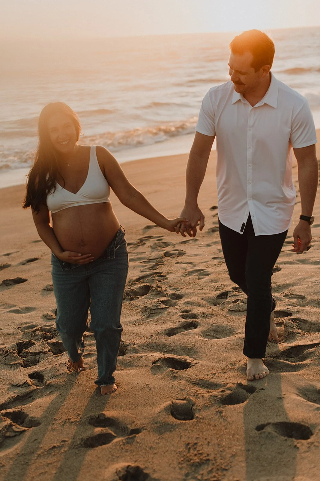 A pregnant woman and a man walking hand in hand on the beach at sunset. Preparing for HypnoBirthing.