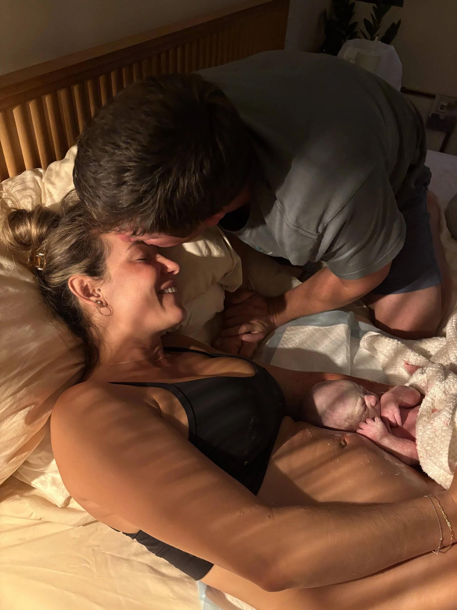 A husband kisses his wife's forehead after she gave birth with the assistance of The Breezy Doula Orange County doula team.