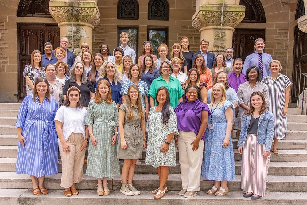 Group photo of diverse adults standing on the steps of a historic building with ornate columns and wooden doors.