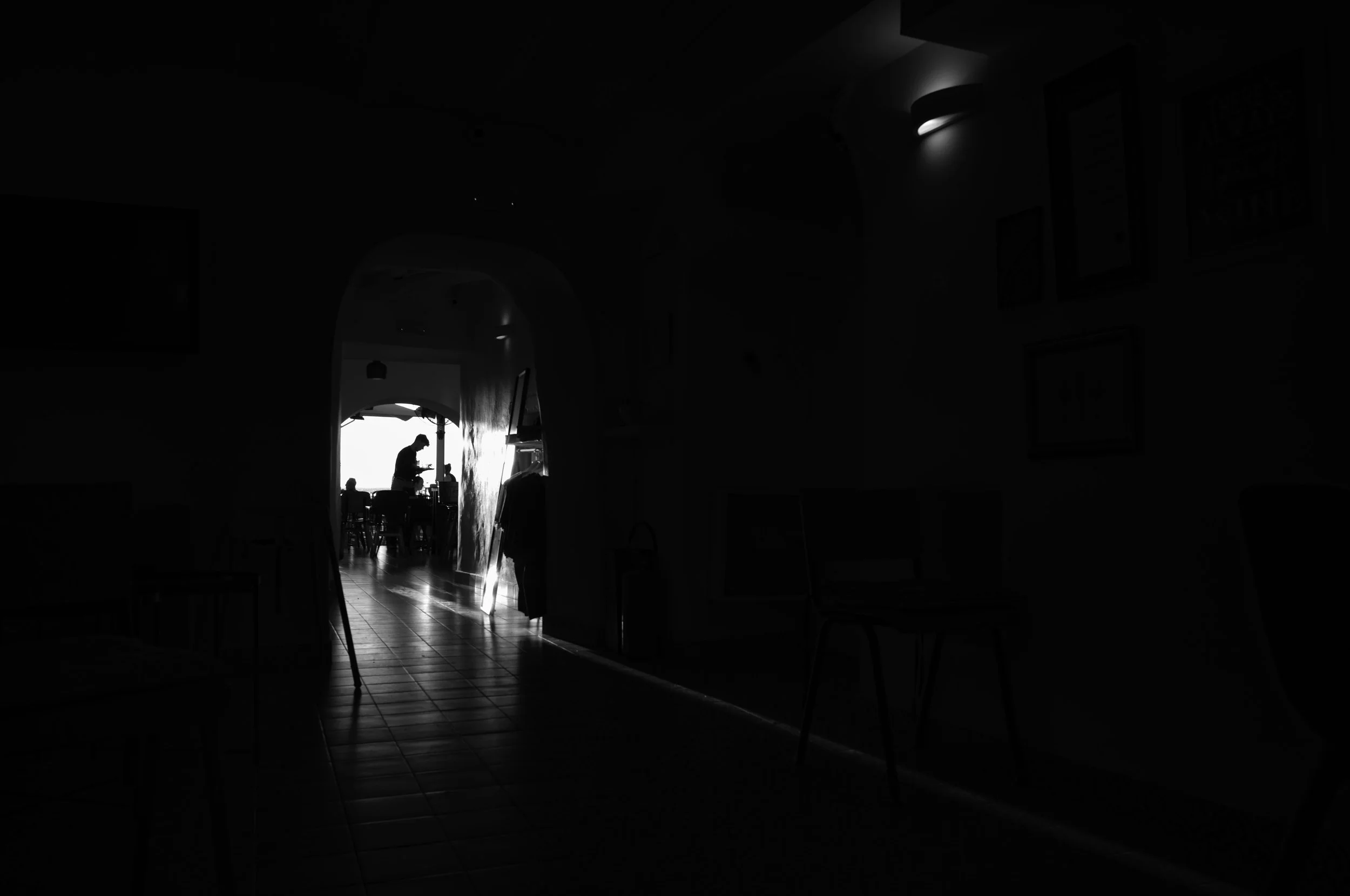 Silhouette of a person standing near a table in a dimly lit room with light coming from an open door or window.