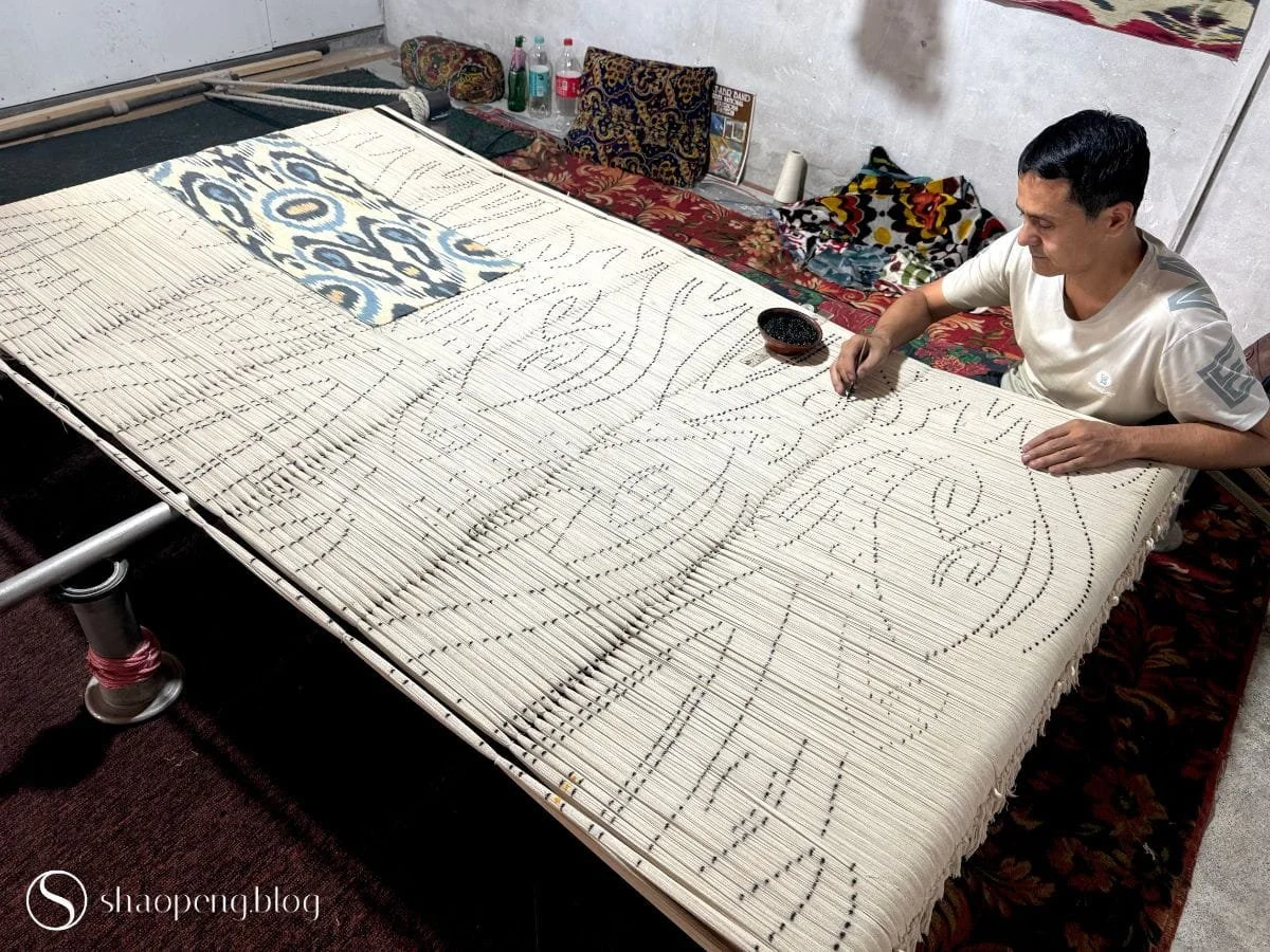 An abrbandchi outlines the pattern on silk warps using charcoal at Silk Factory in Margilan