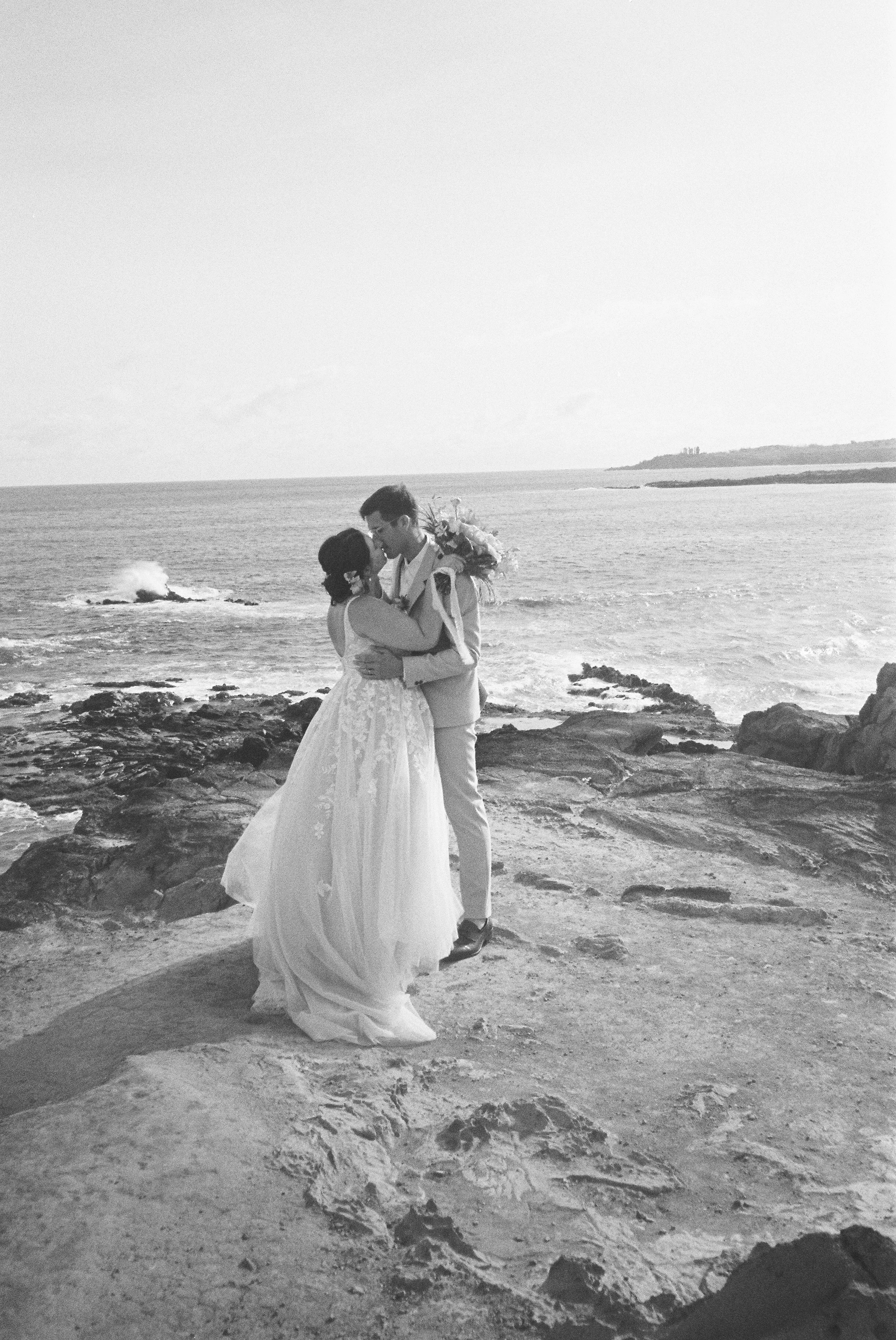 A couple kissing on the rocks at Ironwoods Beach in Maui after their elopement.