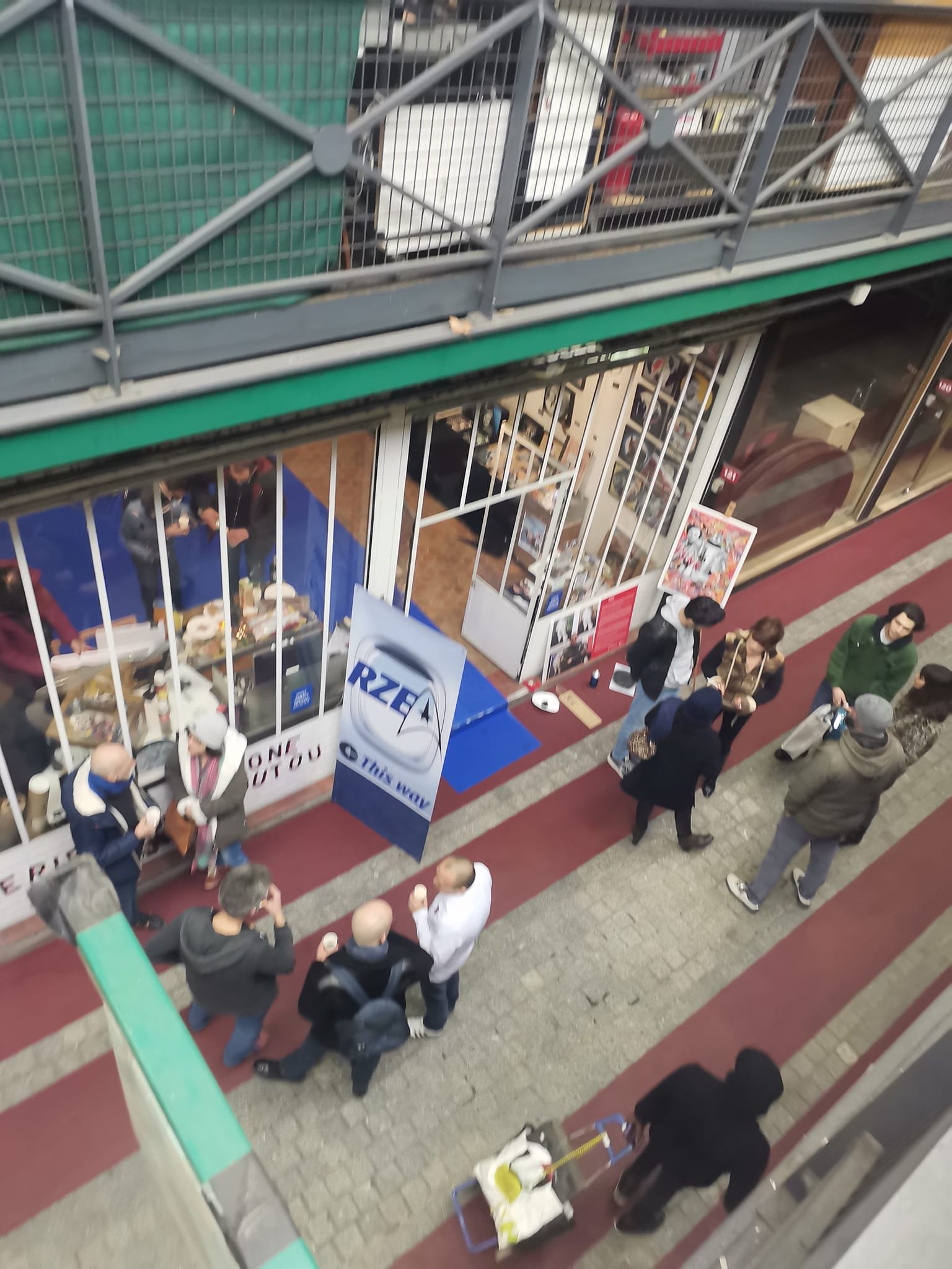 Groupe de personnes faisant la queue devant un stand de nourriture ou de produits lors d'un événement en plein air dans une zone piétonne, vue depuis un angle élevé.
