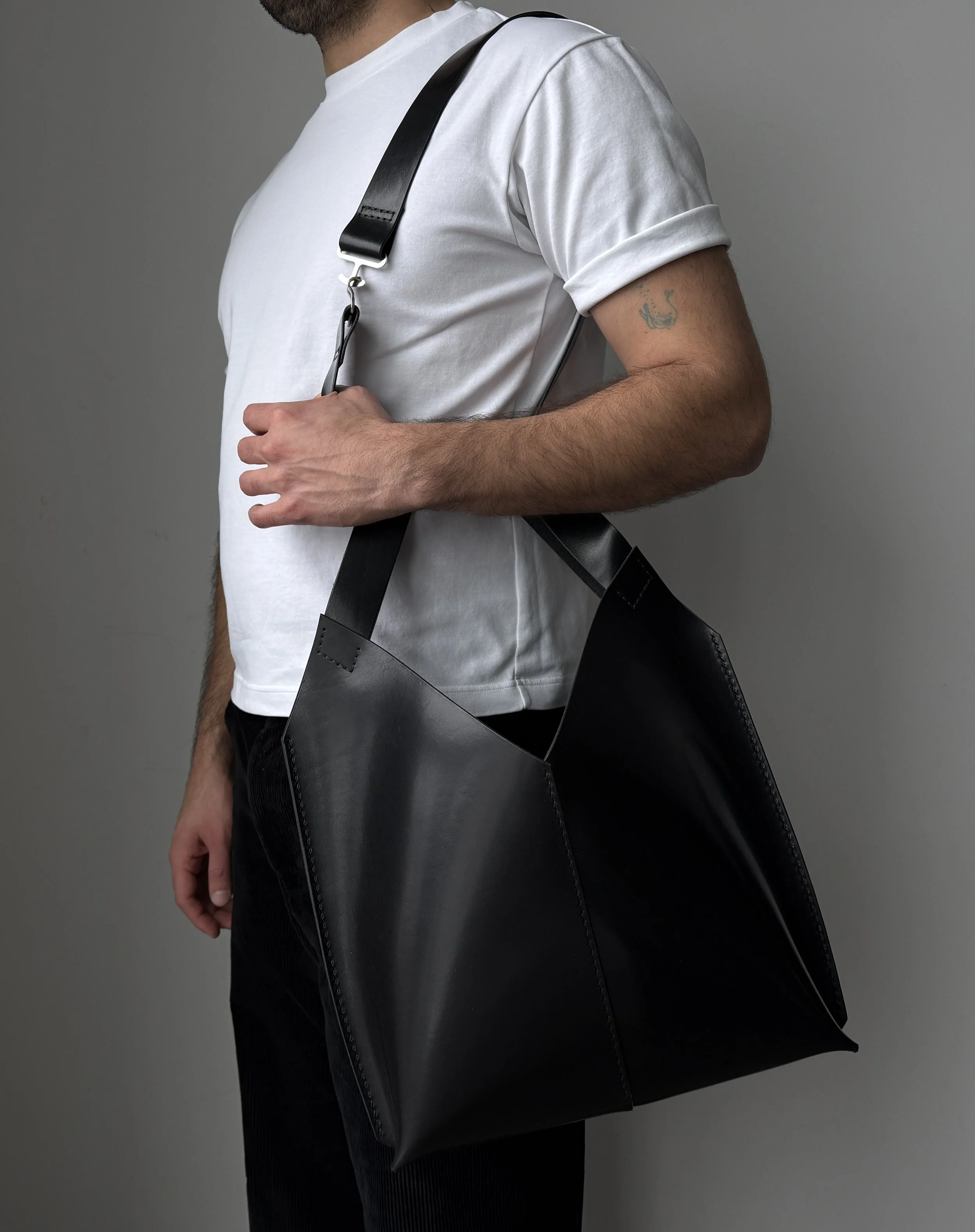 A person wearing a white T-shirt holding a large black tote bag with a shoulder strap.