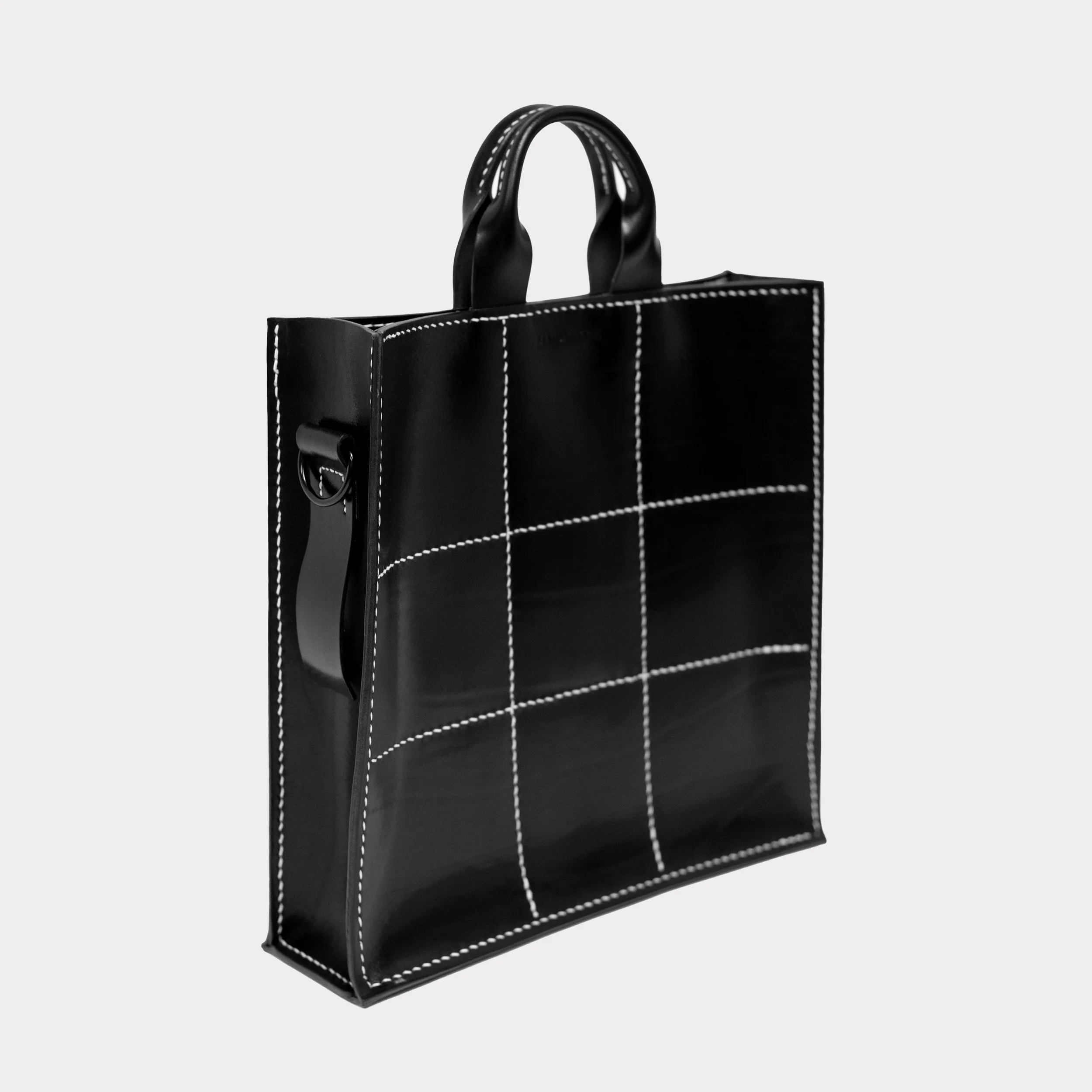 Black tote bag with white stitching pattern, handles, and side strap, on a plain background.