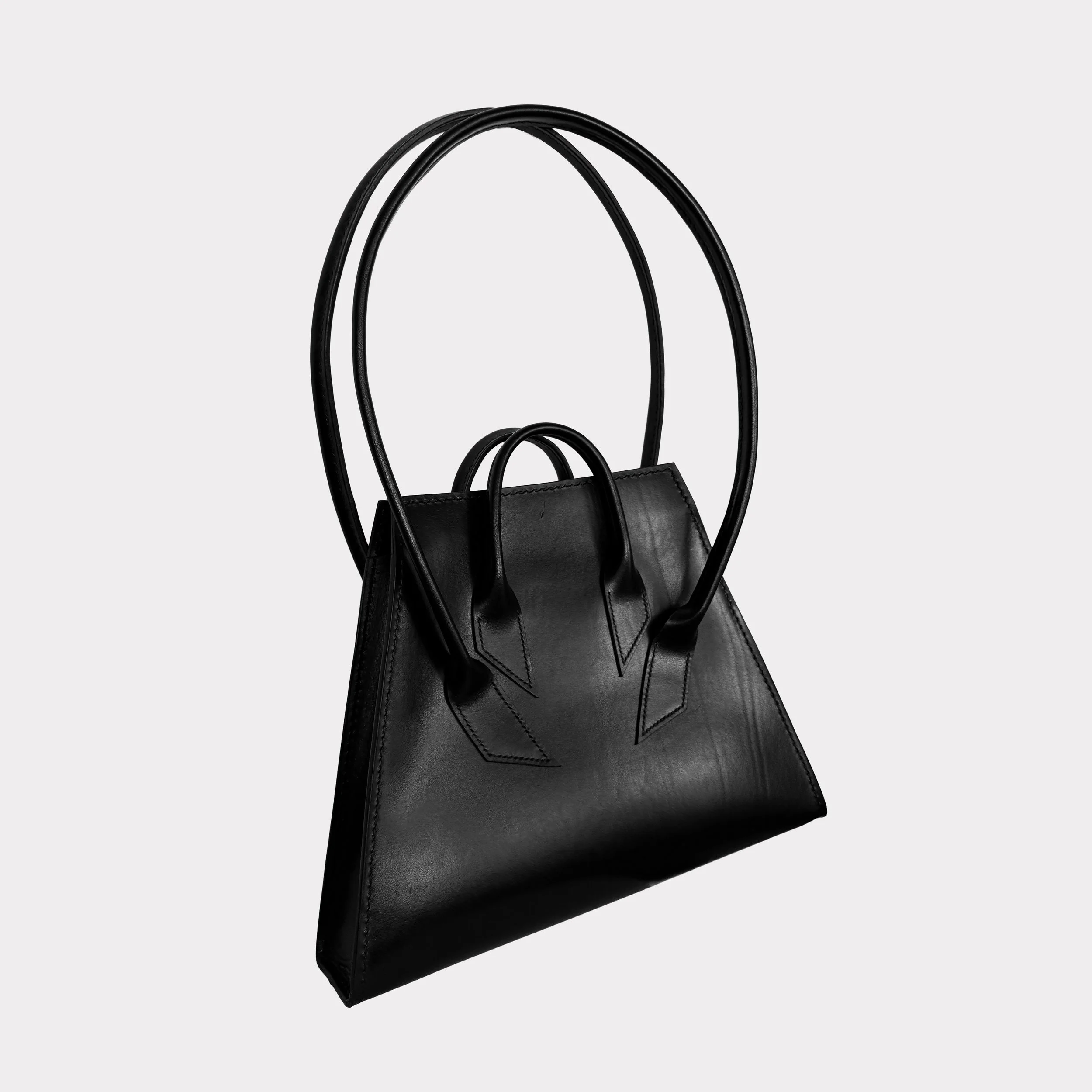 A black leather handbag with structured handles on a plain gray background.