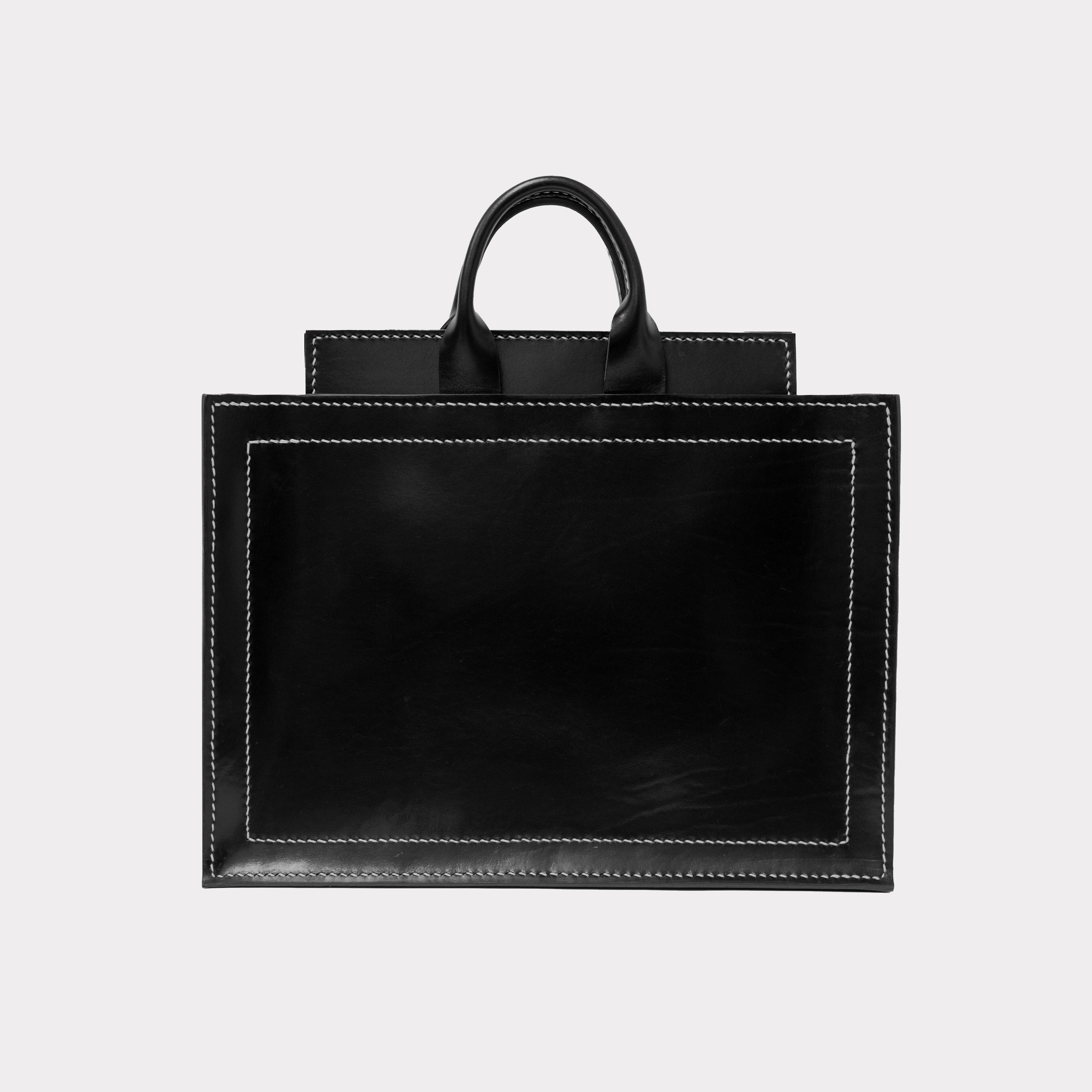 Black leather tote bag with white stitching on a gray background.