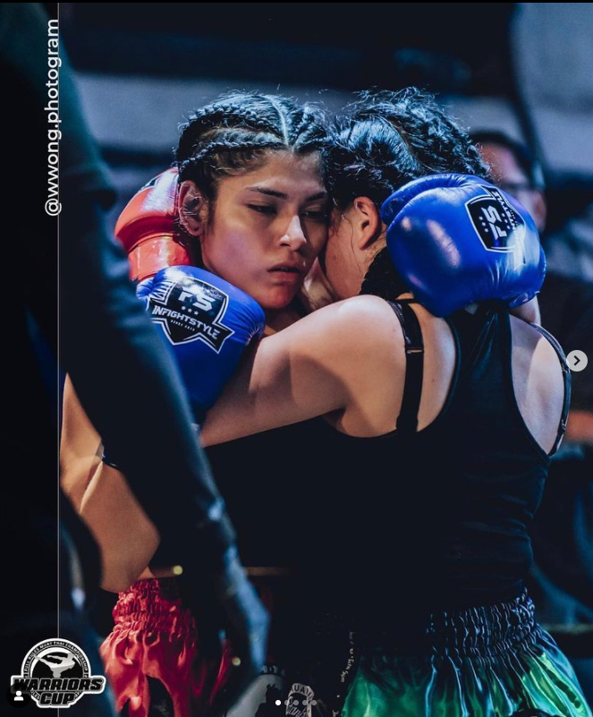 Two female boxers, one with braided hair and one with curly hair, embrace after a match, showing emotion and sportsmanship.