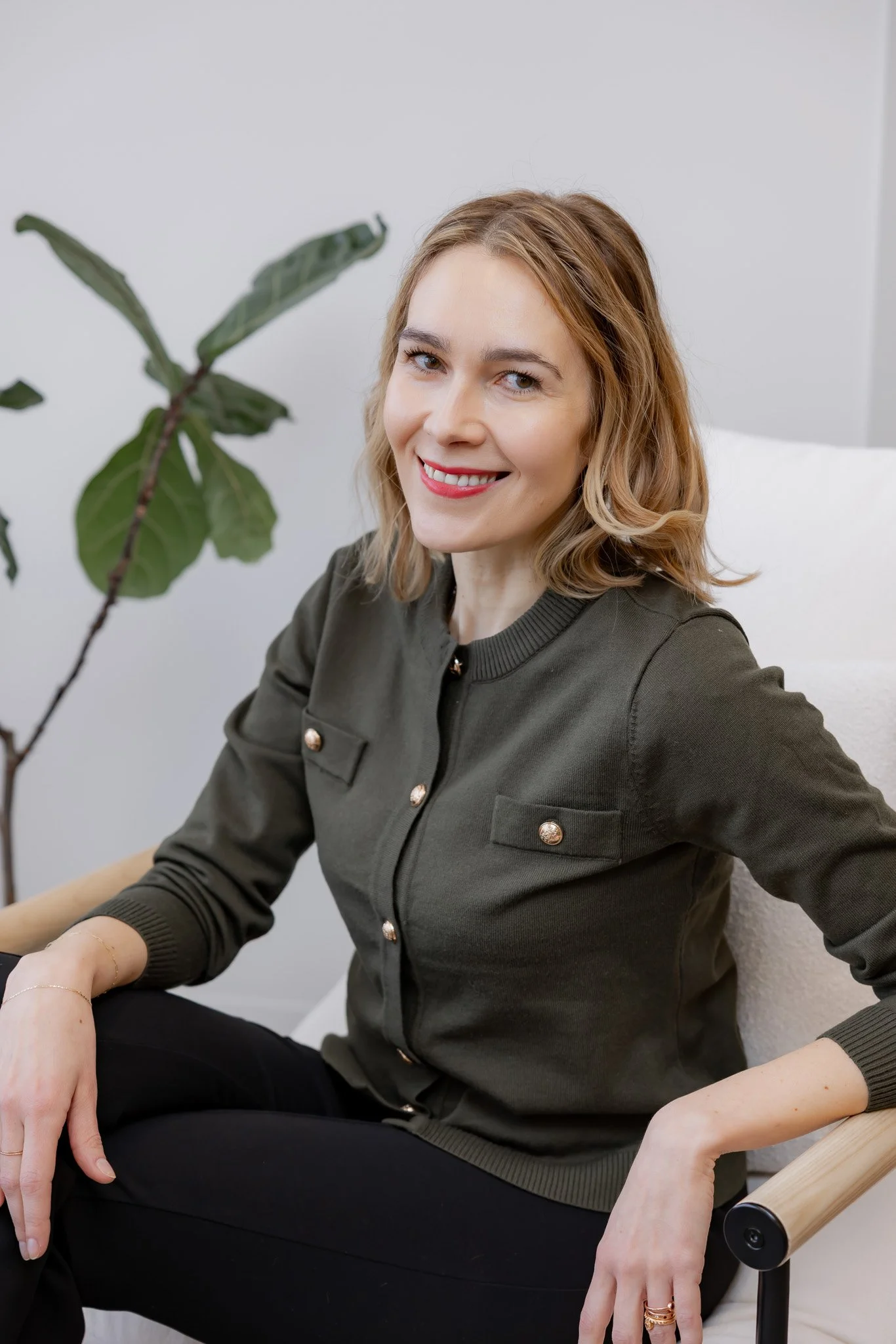 Masha Goins, Head of Programs at Morph Med Spa, seated in a modern chair wearing an olive cardigan, smiling warmly in a bright clinical office setting in Ridgefield, CT.