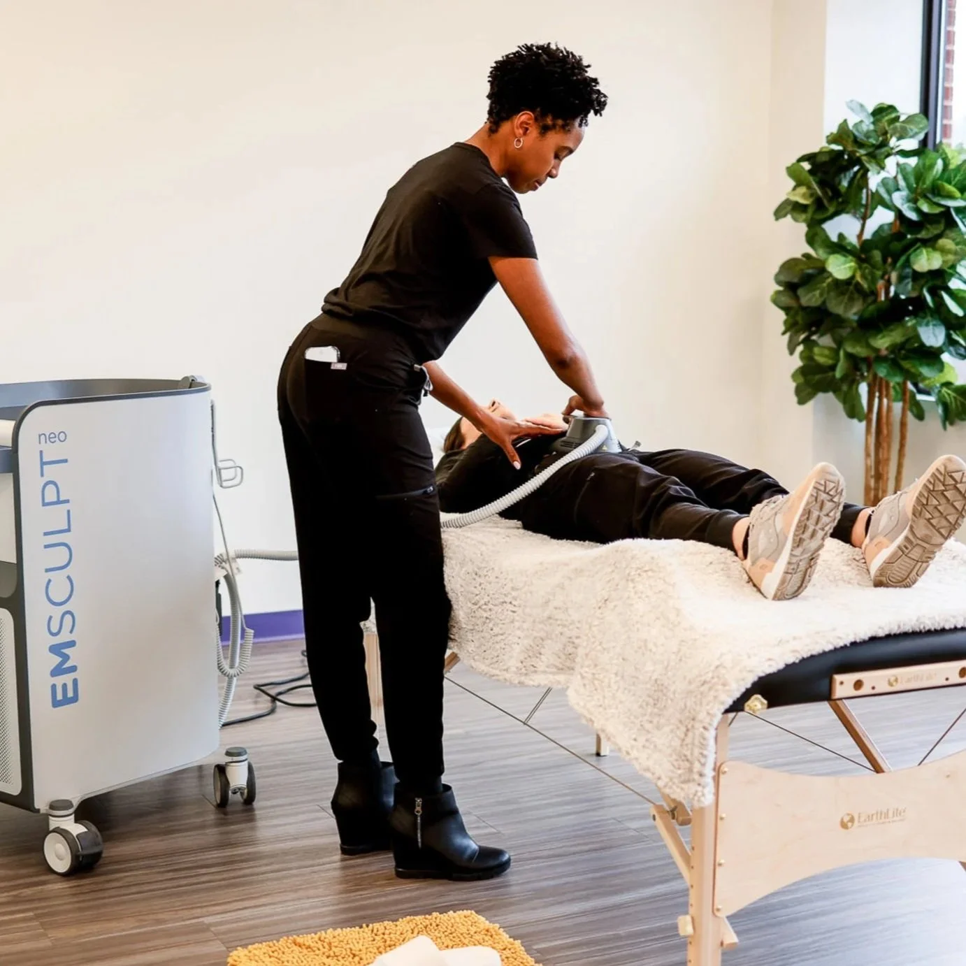 A person receiving a treatment from a healthcare professional in a modern clinic room with large window and indoor plant.