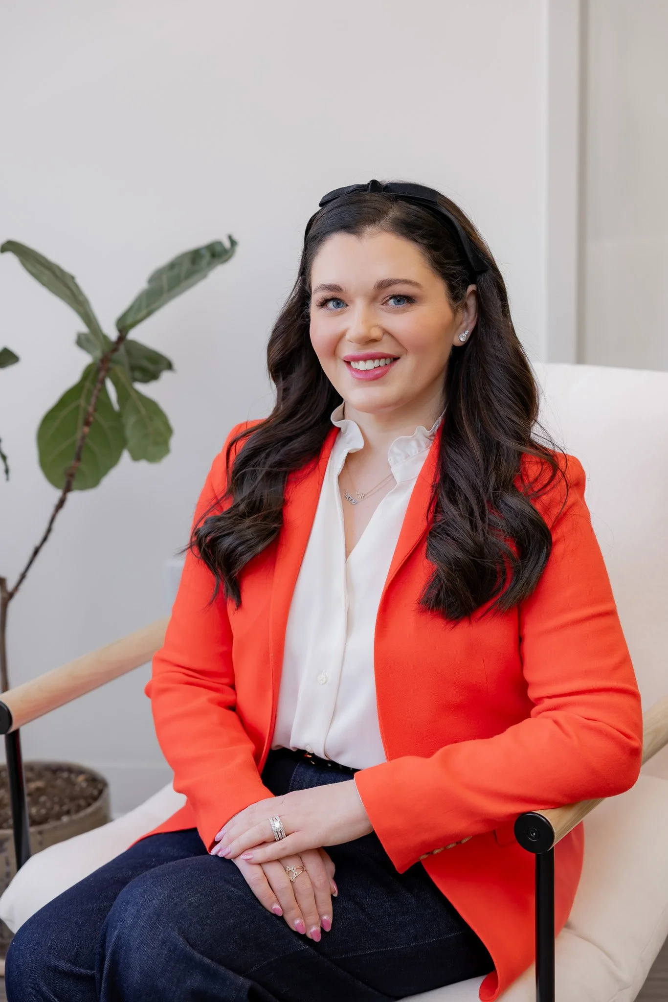Amy Foxman, RN and Medical Aesthetic Provider at Morph Med Spa, seated in a modern chair wearing a red blazer, smiling warmly in a bright clinical office setting.