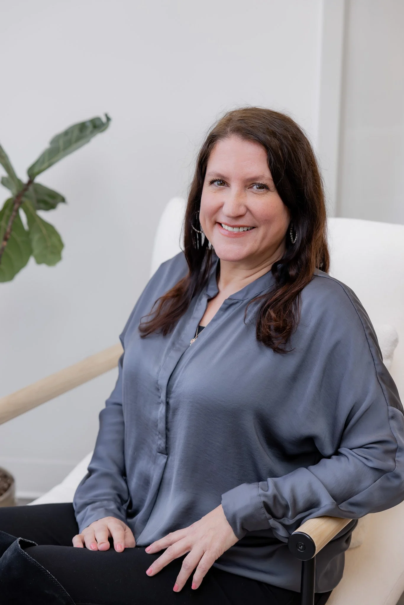 Sarah Luckart, Front of House at Morph Med Spa, seated in a modern chair wearing a gray satin blouse, smiling warmly in a bright office setting in Ridgefield, CT.