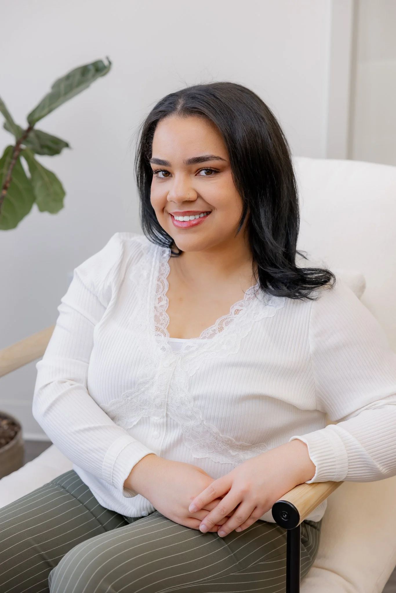 Divine Thomas, Licensed Esthetician at Morph Med Spa, seated in a modern chair wearing a white lace top, smiling warmly in a bright office setting in Ridgefield, CT.