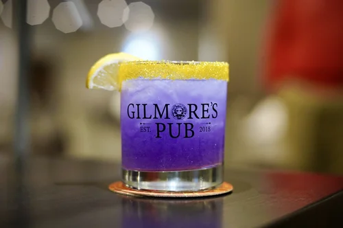 A purple cocktail with a sugar rim in a Gilmore’s Pub glass