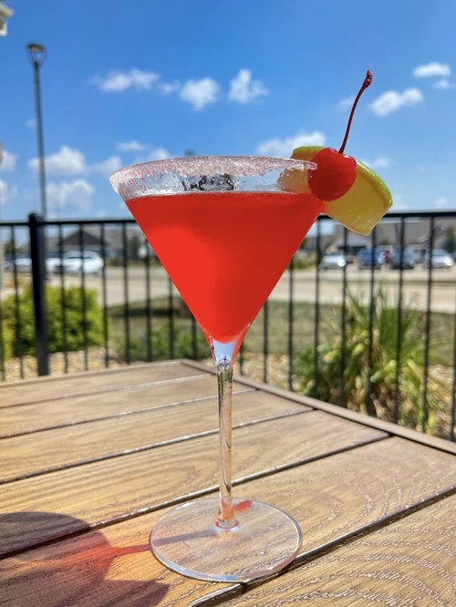 A red cocktail garnished with a cherry and citrus