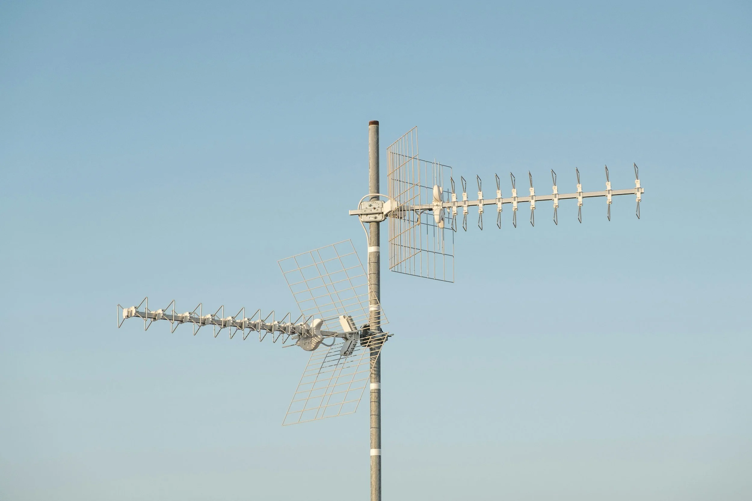 A TV antenna with multiple elements mounted on a pole against a clear blue sky.