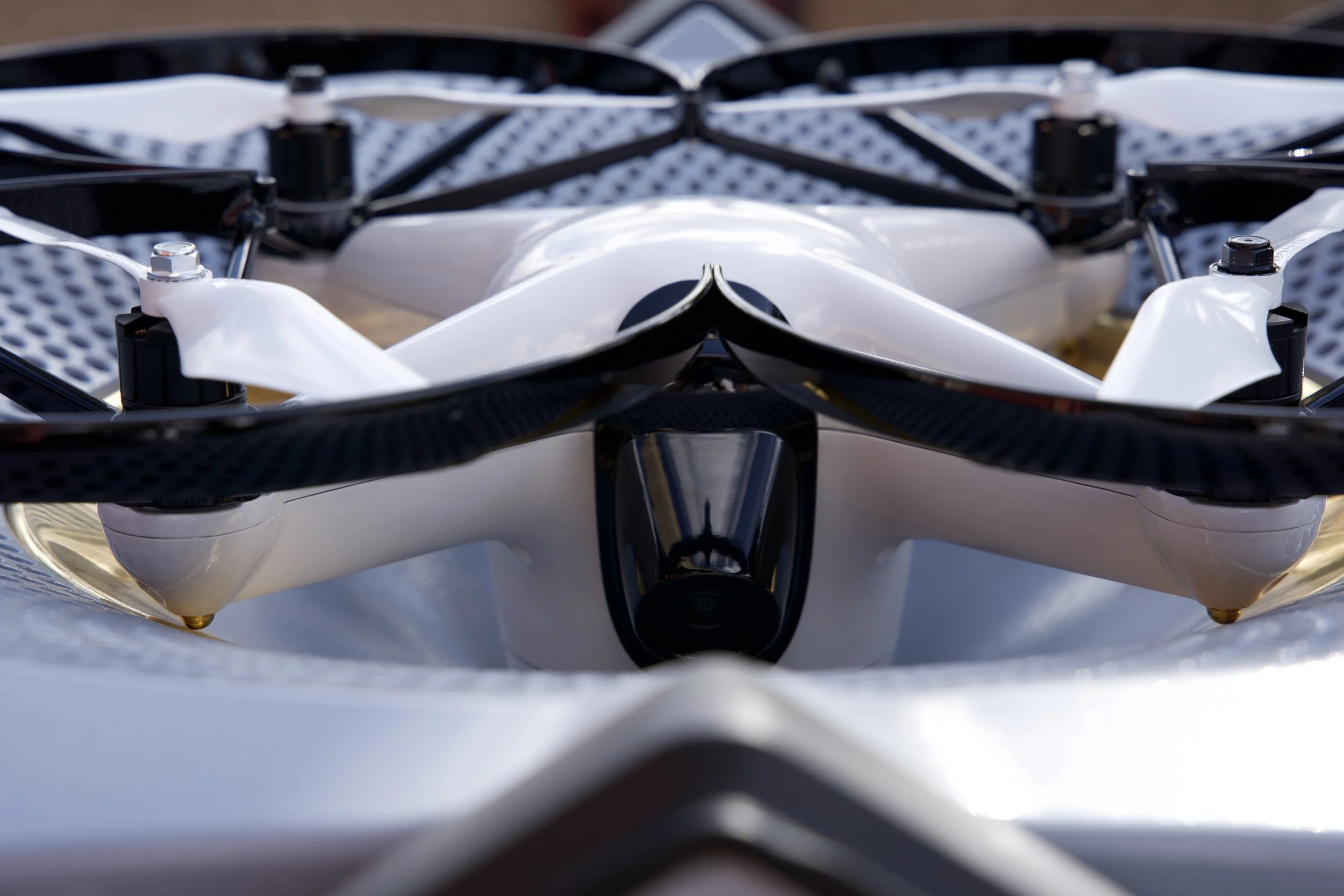 A close-up view of a sleek drone with a camera mounted underneath, resting on a reflective surface.