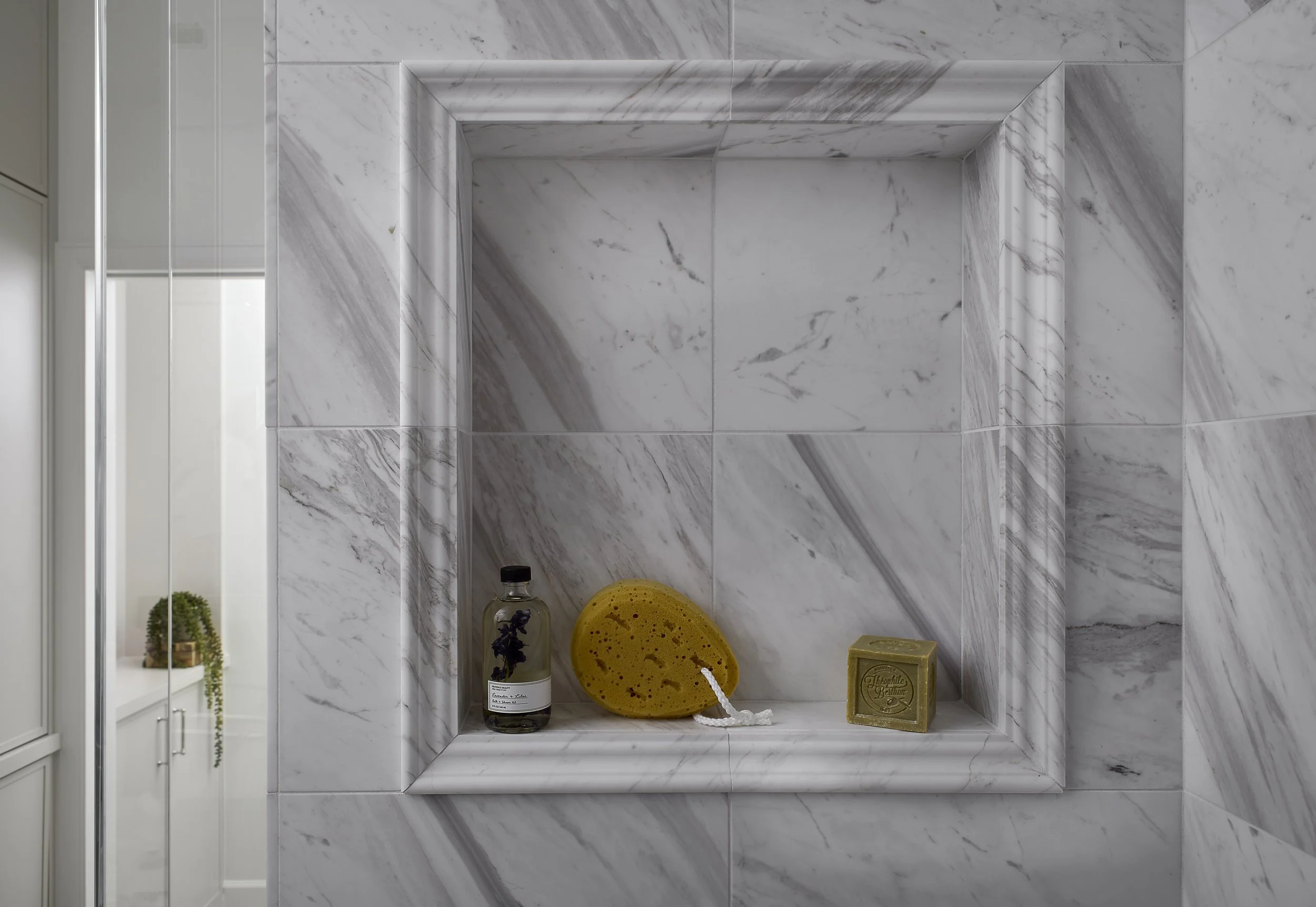 Marble shower niche designed by Flemming Interiors in a Cherry Creek condo renovation, featuring integrated stone detailing and a framed recessed shelf within the primary bathroom.