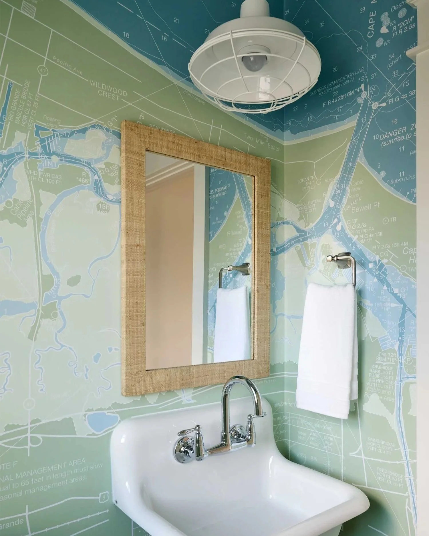 Nautical wallpaper in small bathroom with white sink and light fixture.