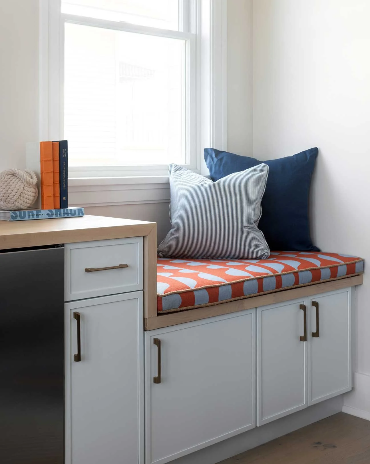 A cozy window seat with white cabinets and colorful cushions next to a window.