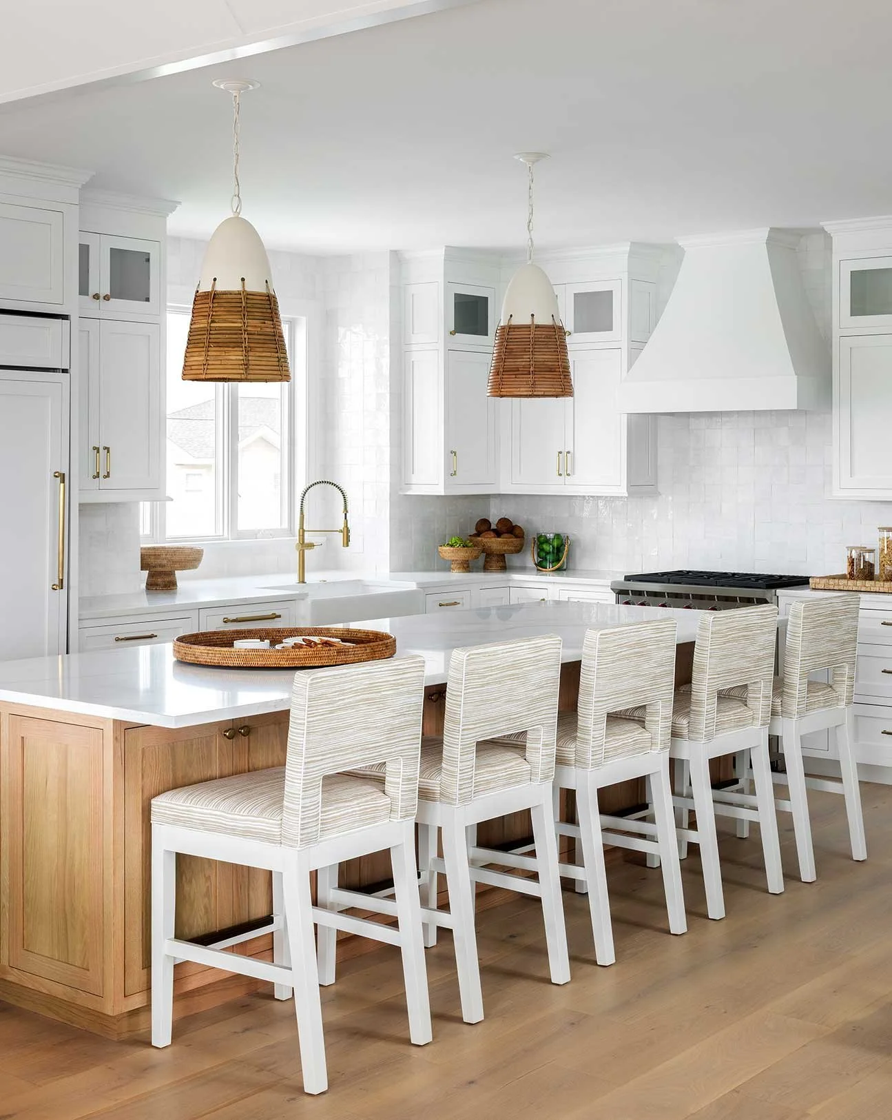 Modern white kitchen with island and seven bar stools, pendant lights, and cabinetry.